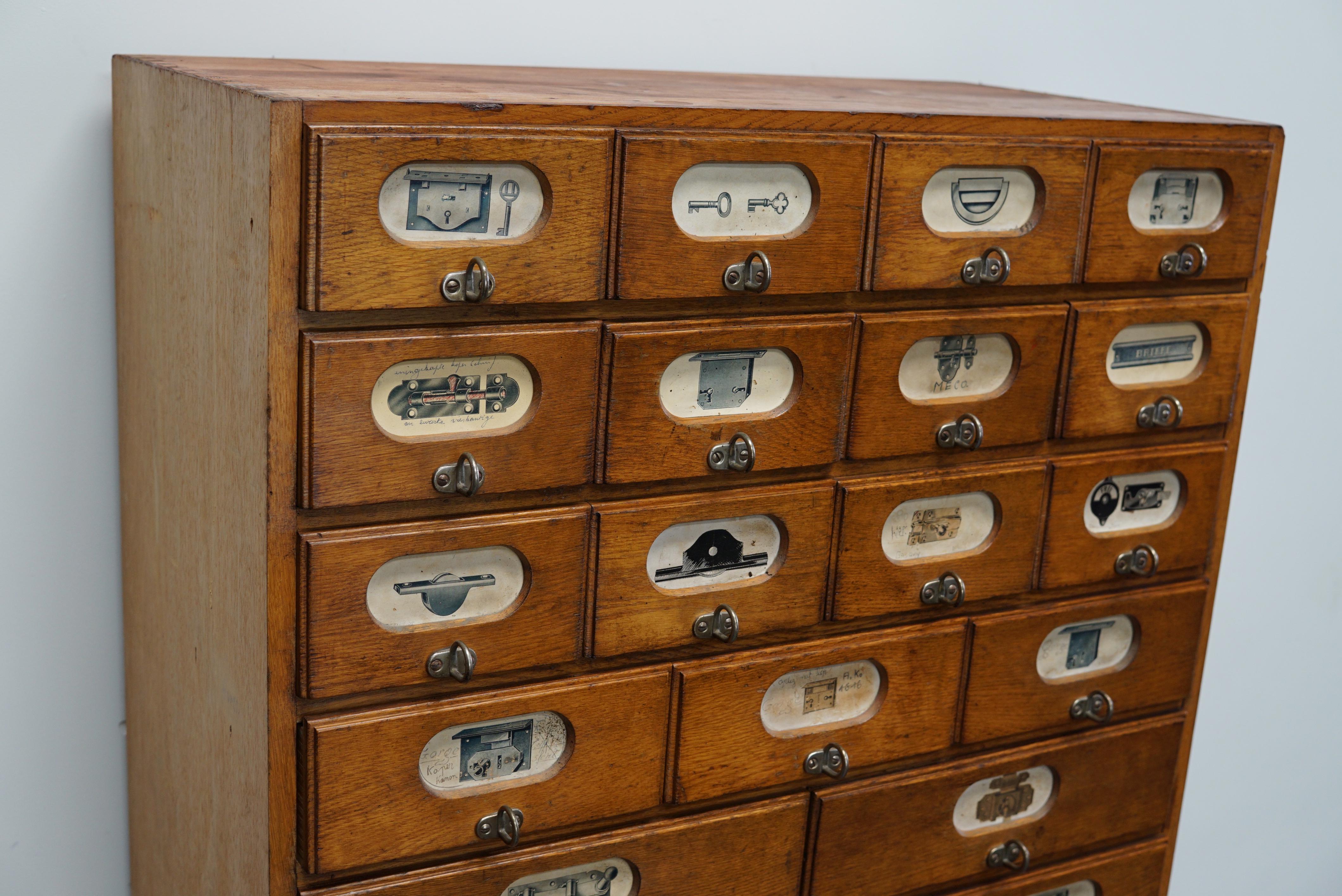 This apothecary cabinet was made circa 1940s in Germany and was later used in a hardware store in Belgium until recently. It features many drawers in different sizes with metal handles and the labels of the contents.