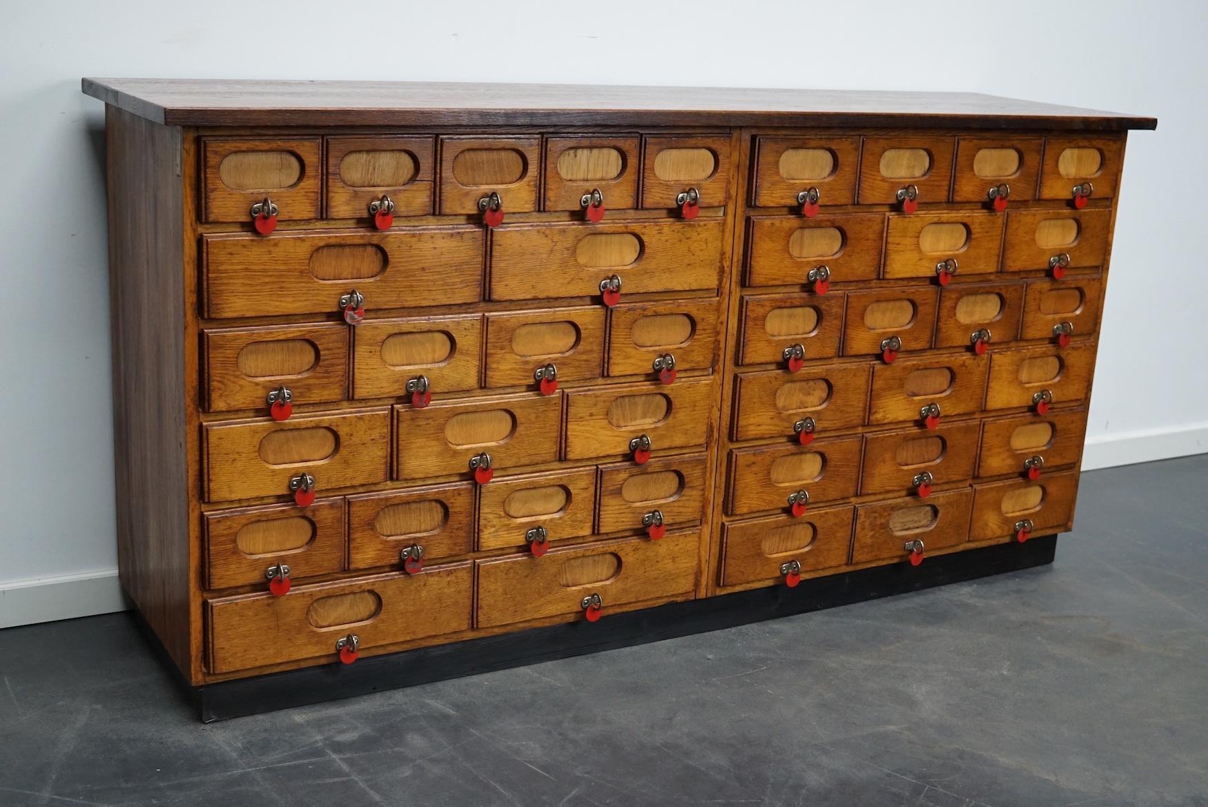 This apothecary cabinet was made circa 1940s in Germany and was later used in a hardware store in Belgium until recently. It features many drawers in different sizes with metal handles. The red coins were used to show that products were out of stock.