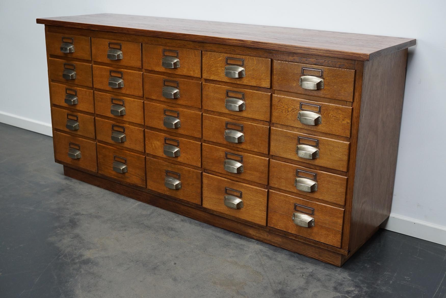 This apothecary cabinet was made from oak circa 1940 / 1950s in Germany. It features 24 drawers with nice metal handles and name card holders. The interior dimensions of the drawers are: D W H 36.5 x 25 x 8 and 12 cm. Two of the drawers are joint