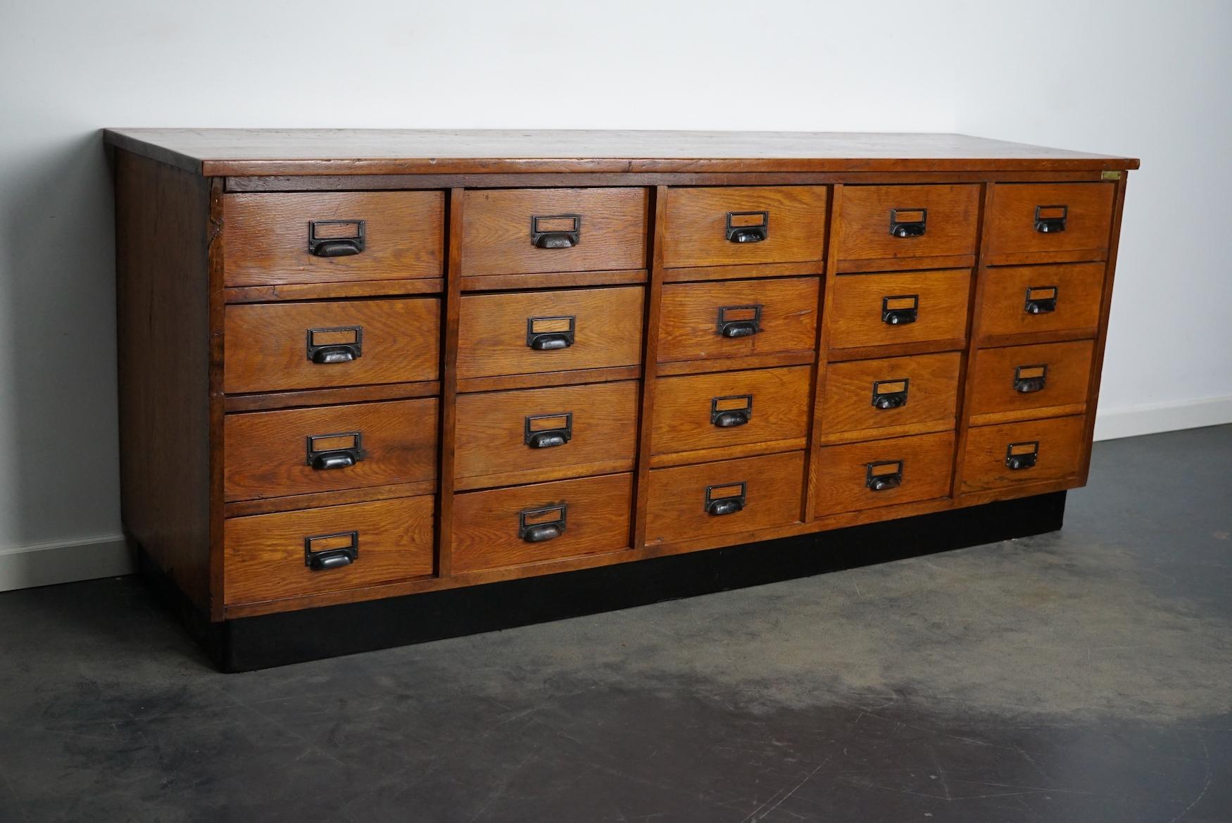 This apothecary cabinet was designed and made from oak ply, pine and hardwood circa 1950 in Germany. It features 20 drawers with black metal hardware. The inside of the drawers measure: DWH 44 x 30 x 11 cm.