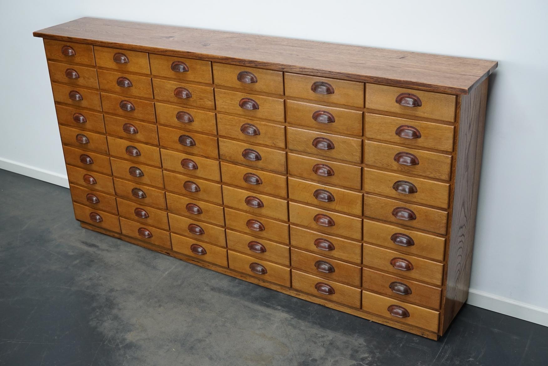 This apothecary cabinet was made from oak circa 1940 / 1950s in Germany. It features 54 drawers with nice metal handles. The interior dimensions of the drawers are: DWH 26 x 28 x 7 cm. We have a pair of these cabinets available.