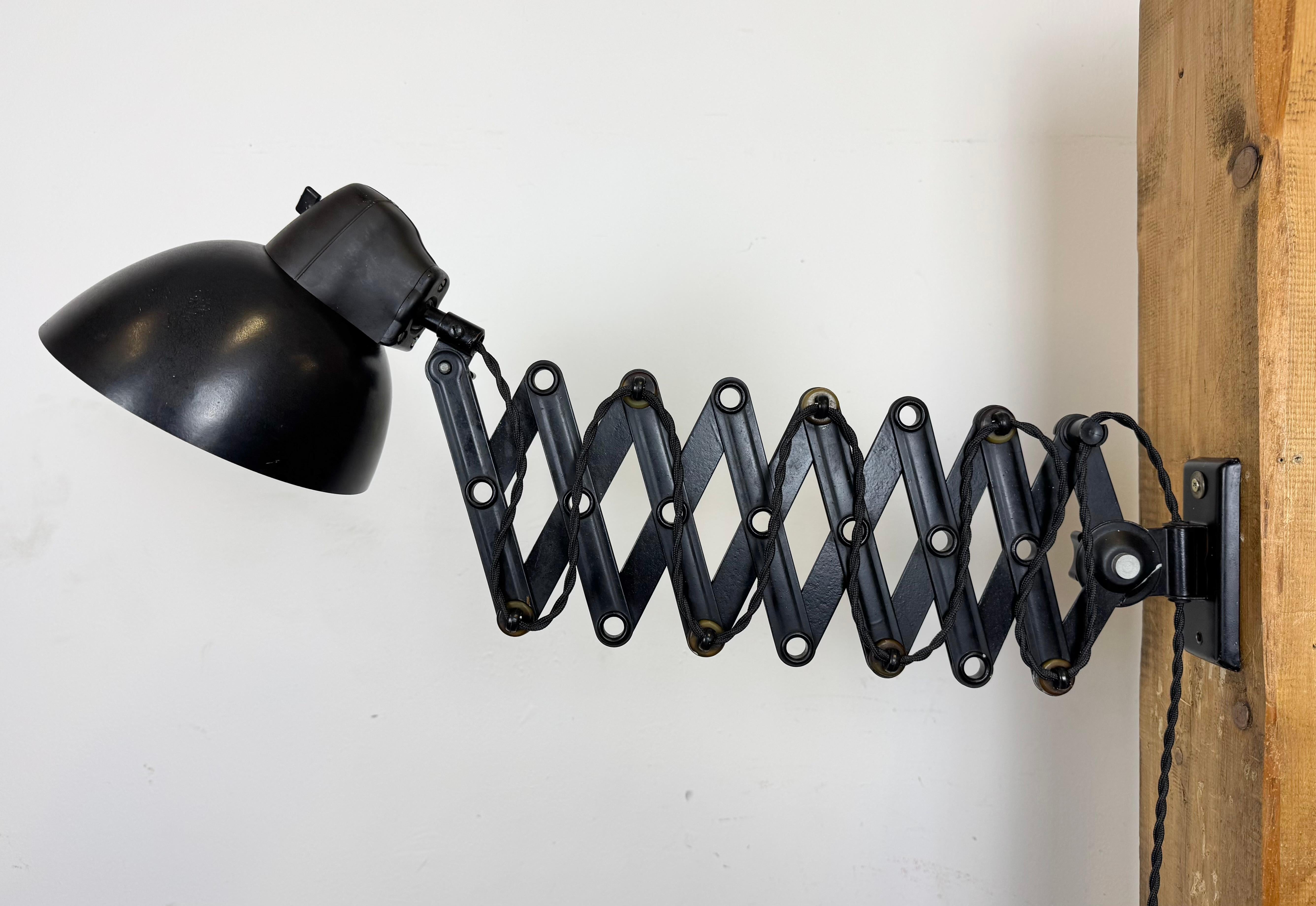 This vintage industrial adjustable scissor lamp was produced by LBL, Leuchtenbau Leipzig in Germany during the 1950s The lamp has dark brown bakelite lampshade. Black iron scissor arm is extendable and can be turned sideways. The original socket