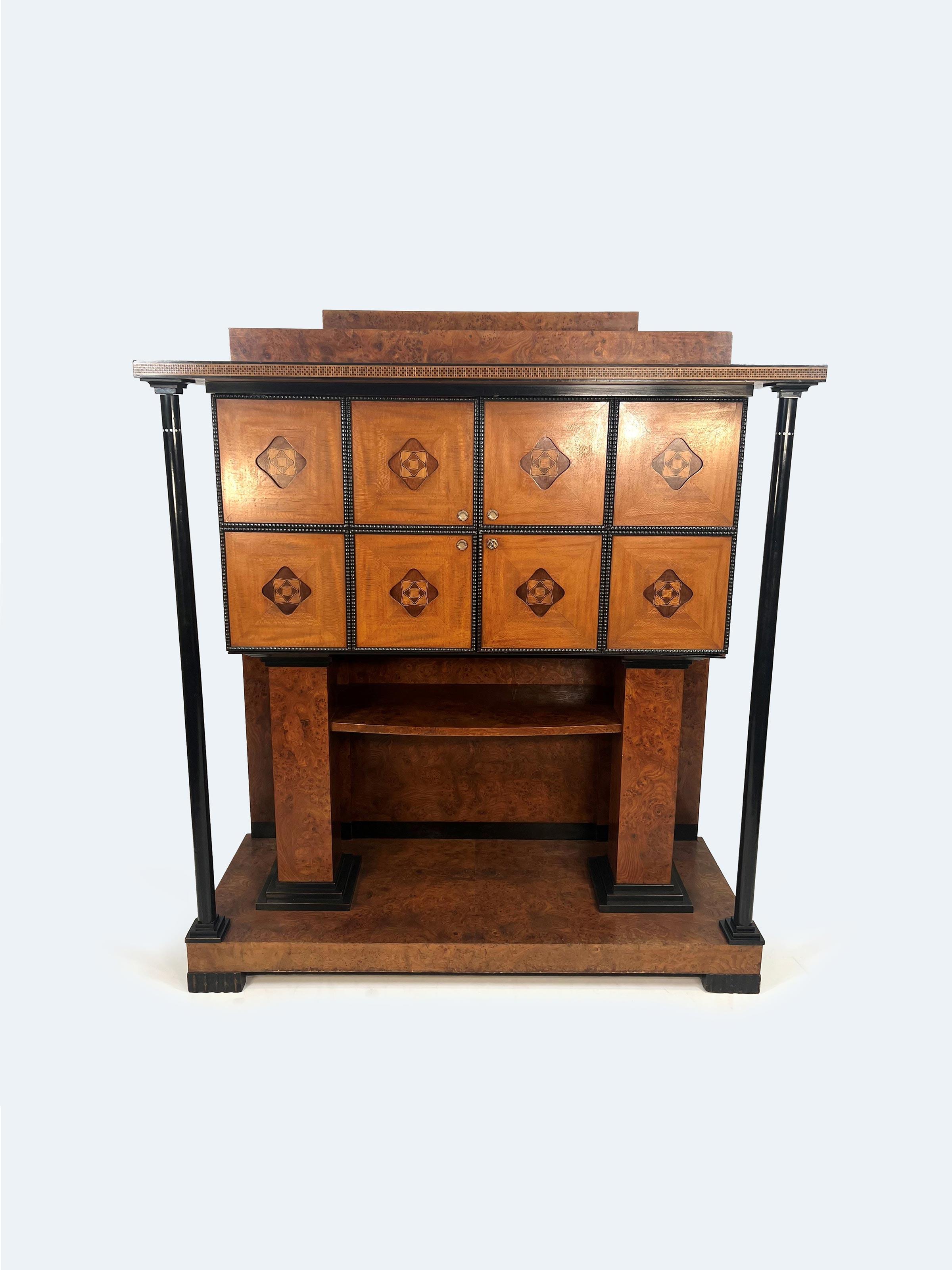 The music room cabinet by Joseph Maria Olbrich, attributed to the cabinetmaker Heinrich Julius Glückert, stands as a masterpiece of craftsmanship and design, showcasing a stunning fusion of luxurious wood veneers and intricate detailing. Crafted