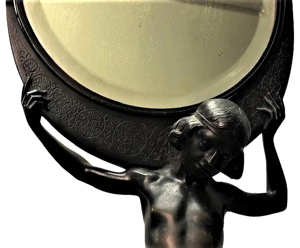 Heavy and graceful sculptural table make-up mirror in the Jugenstil style. Made of black-patinated bronze in the shape of a slender young man holding a round mirror on his shoulders. The round mirror part rotates full 360 degrees around its axis,