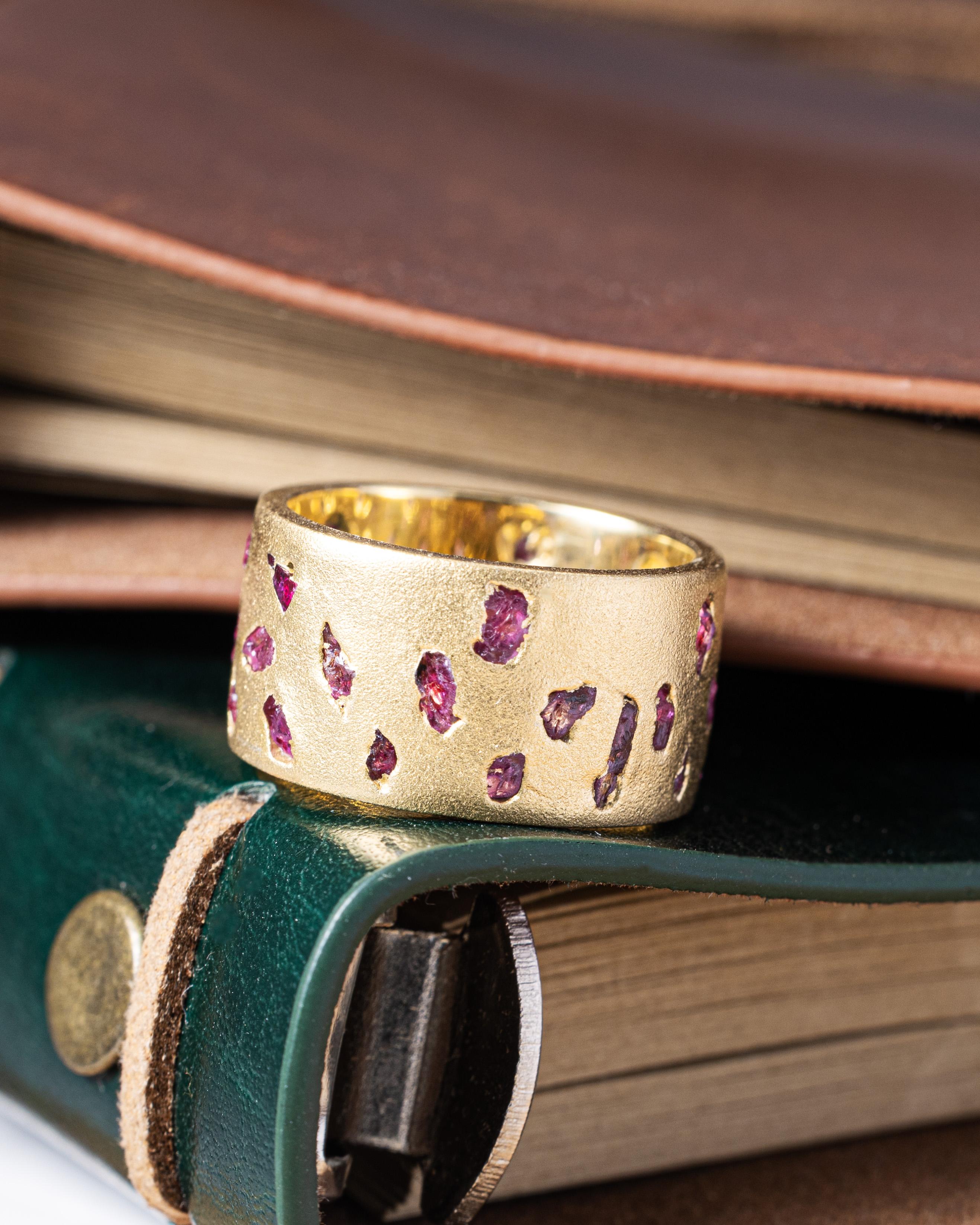 Carisa è un anello a barile realizzato a mano e ricoperto di pezzi di rubino grezzo incastonati direttamente nel metallo. I rubini sono disposti intorno alla fascia, ognuno nella sua forma naturale, senza essere lucidati o modellati. Le loro