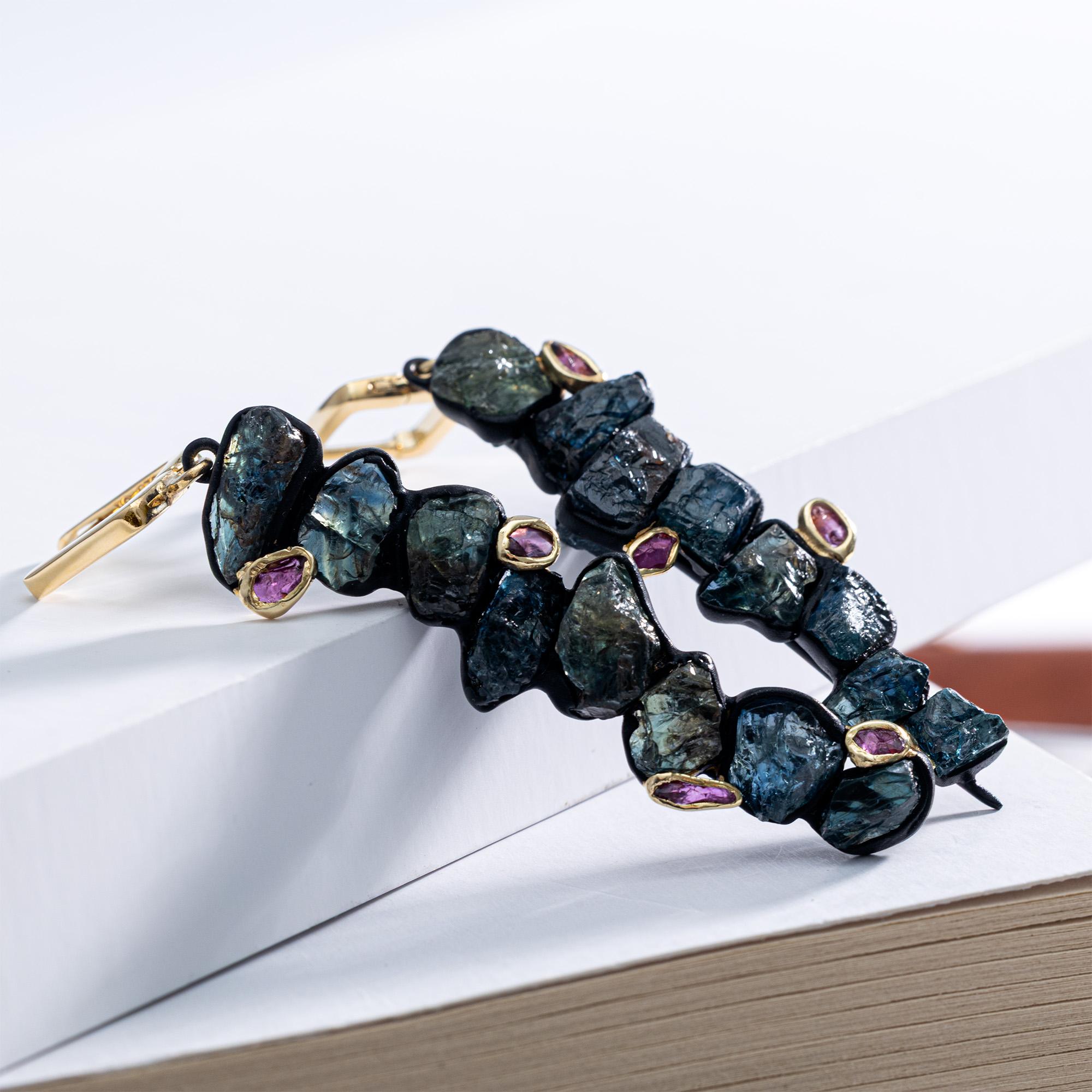 Danae unisce lo zaffiro blu grezzo e il rubino grezzo in una forma di orecchino lunga e fluida. Gli zaffiri si susseguono in una linea verticale allungata e i rubini li affiancano in modo naturale e non pianificato: ogni pietra è grezza, con la sua