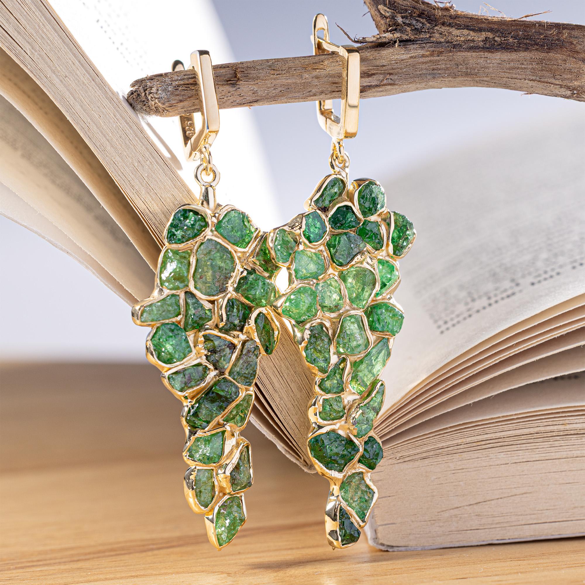 Tarina è per coloro che vogliono le pietre preziose nella loro forma più naturale e incontaminata. Questi orecchini presentano un grande grappolo pendente di cristalli di Tsavorite grezzi disposti in una goccia simile a un chicco d'uva che si muove