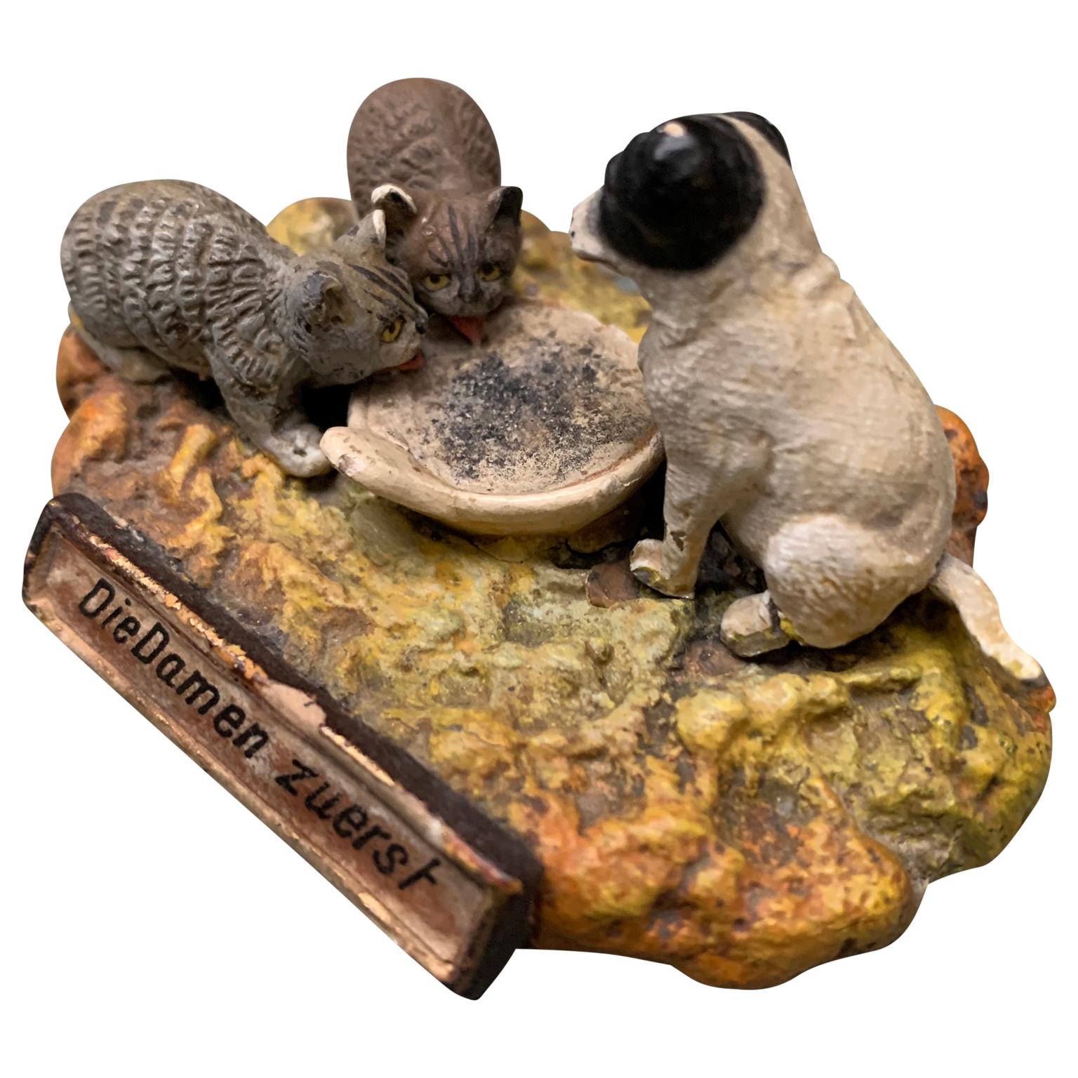 A group of small wiener bronze style figurines in metal and plaster illustrating pets eating. The German text of 