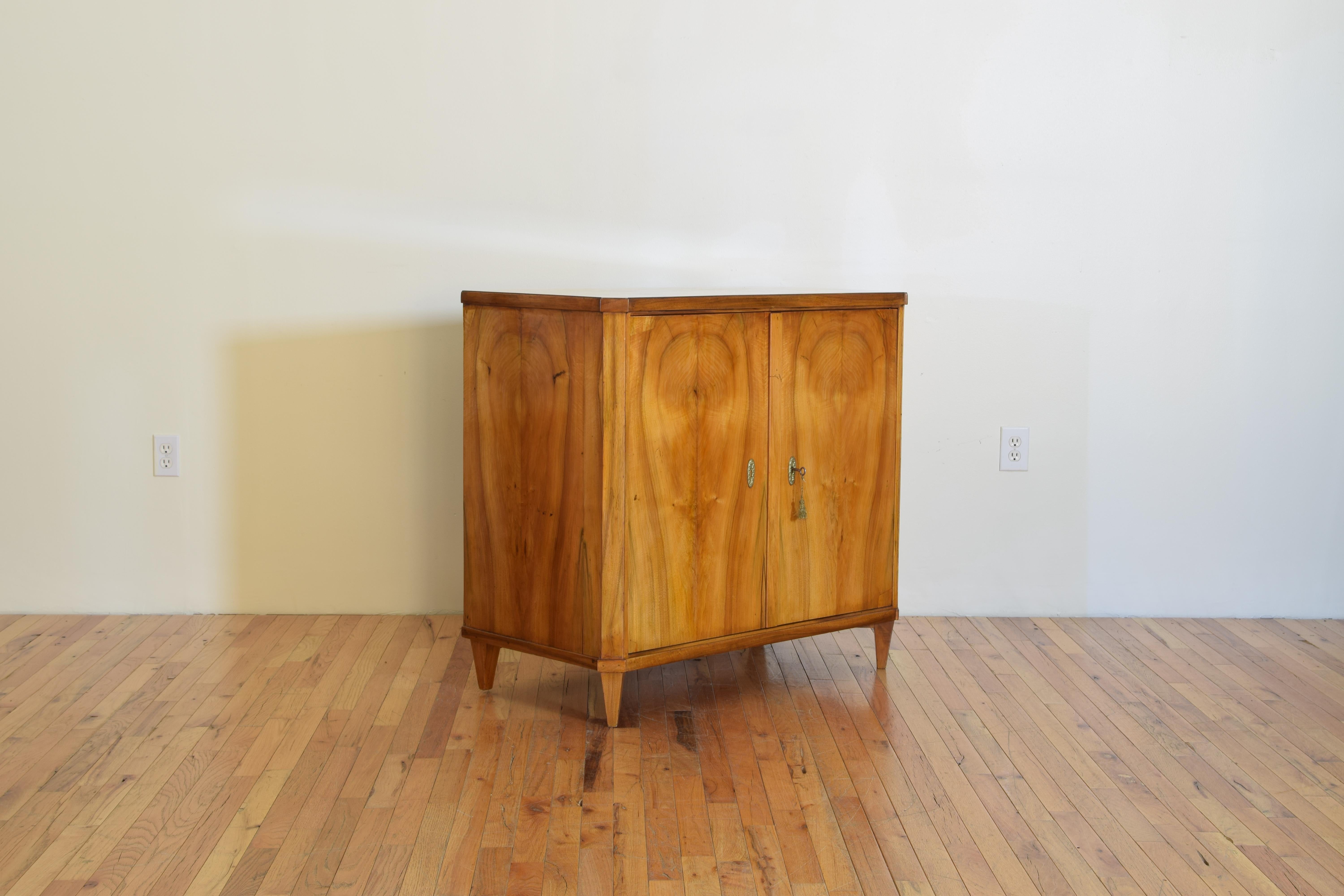 The rectangular top with front canted corners above a conforming case with matched grain veneers, the interior with adjustable shelf, raised on tapered legs.