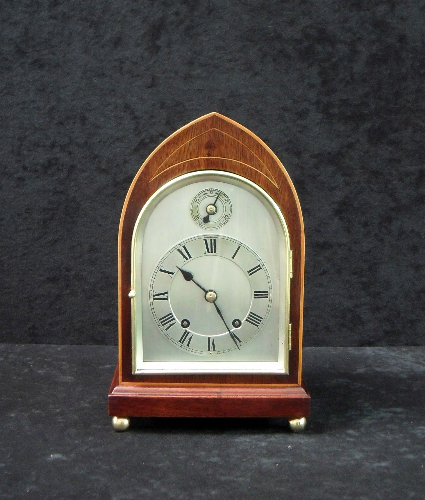 A very good quality late Victorian figured mahogany lancet top mantel clock with boxwood stringing to the front of the case stood on brass ball feet.

The clock has a silvered dial with a slow-fast mechanism and has a German Winterhalder &
