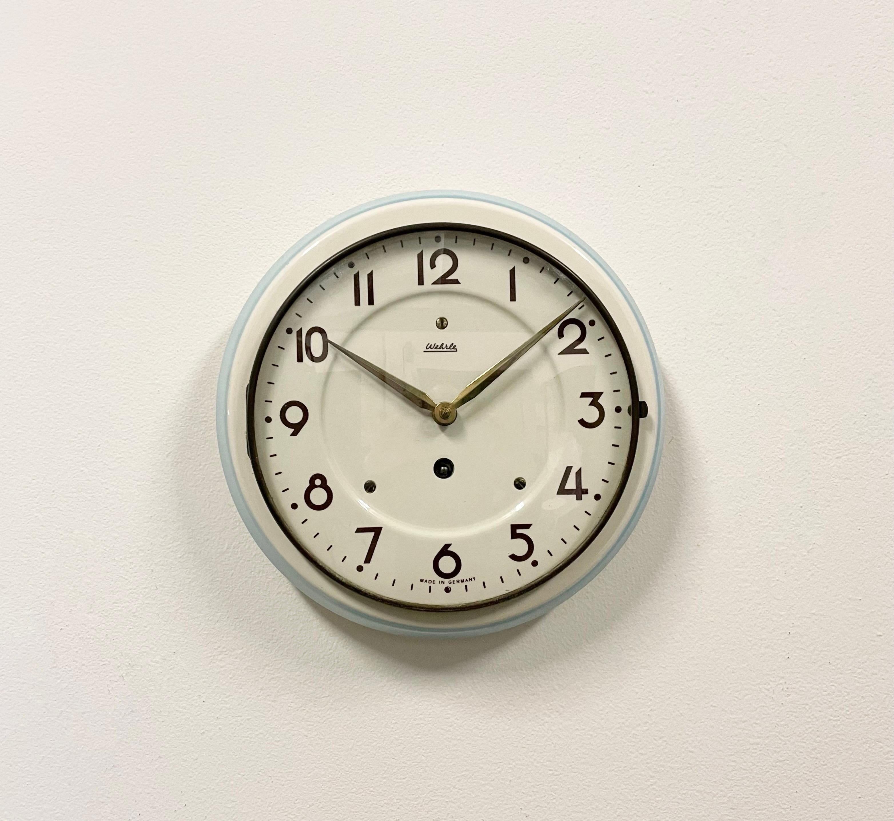 Vintage ceramic winding kitchen wall clock made by Wehrle in Germany during the 1960s.It features a white and blue ceramic body and a convex clear glass cover with brass frame. The original mechanic movement works perfectly. Key included. Very good