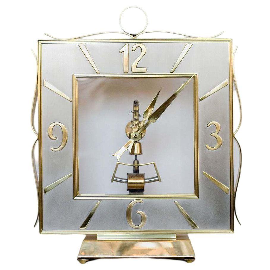 A stunning Mid-Century/Hollywood Regency styled mantel clock with a brass case and floating glass paneled center stage with an electromagnetic movement, with a brushed steel square chapter ring with a Roman numeral chapter ring and pierced