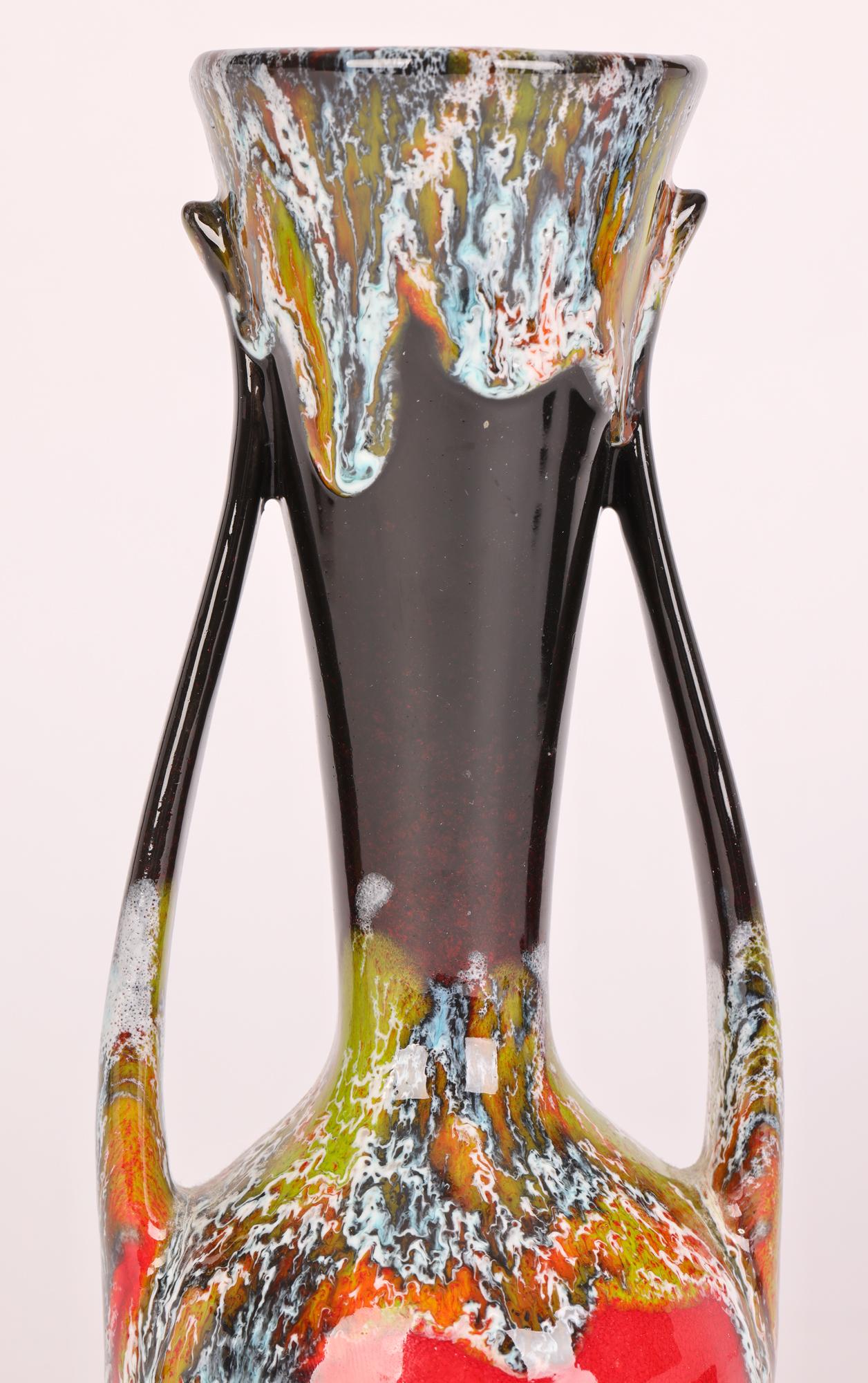 A very stylish German mid-century twin handled vase decorated with colored dripped glazes over a red and black glazed ground. This stunning vase is well potted and stands on a narrow round unglazed foot with slightly recessed red glazed base. With a