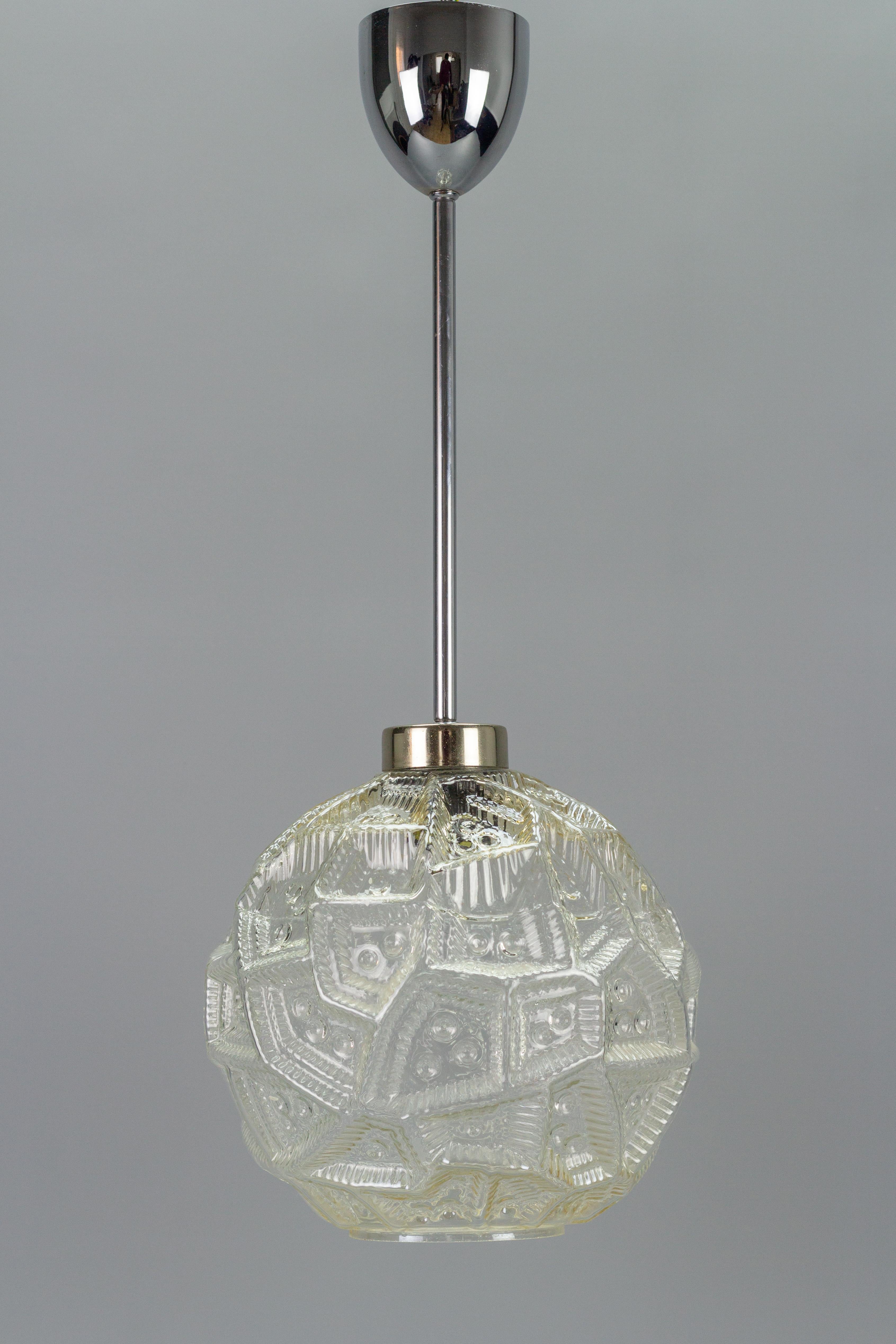 Lampe à suspension moderne du milieu du siècle avec abat-jour en verre transparent et fixation chromée. Allemagne, années 1970. La lumière se reflète et se réfracte magnifiquement sur la texture inhabituelle de la surface du globe en verre, créant