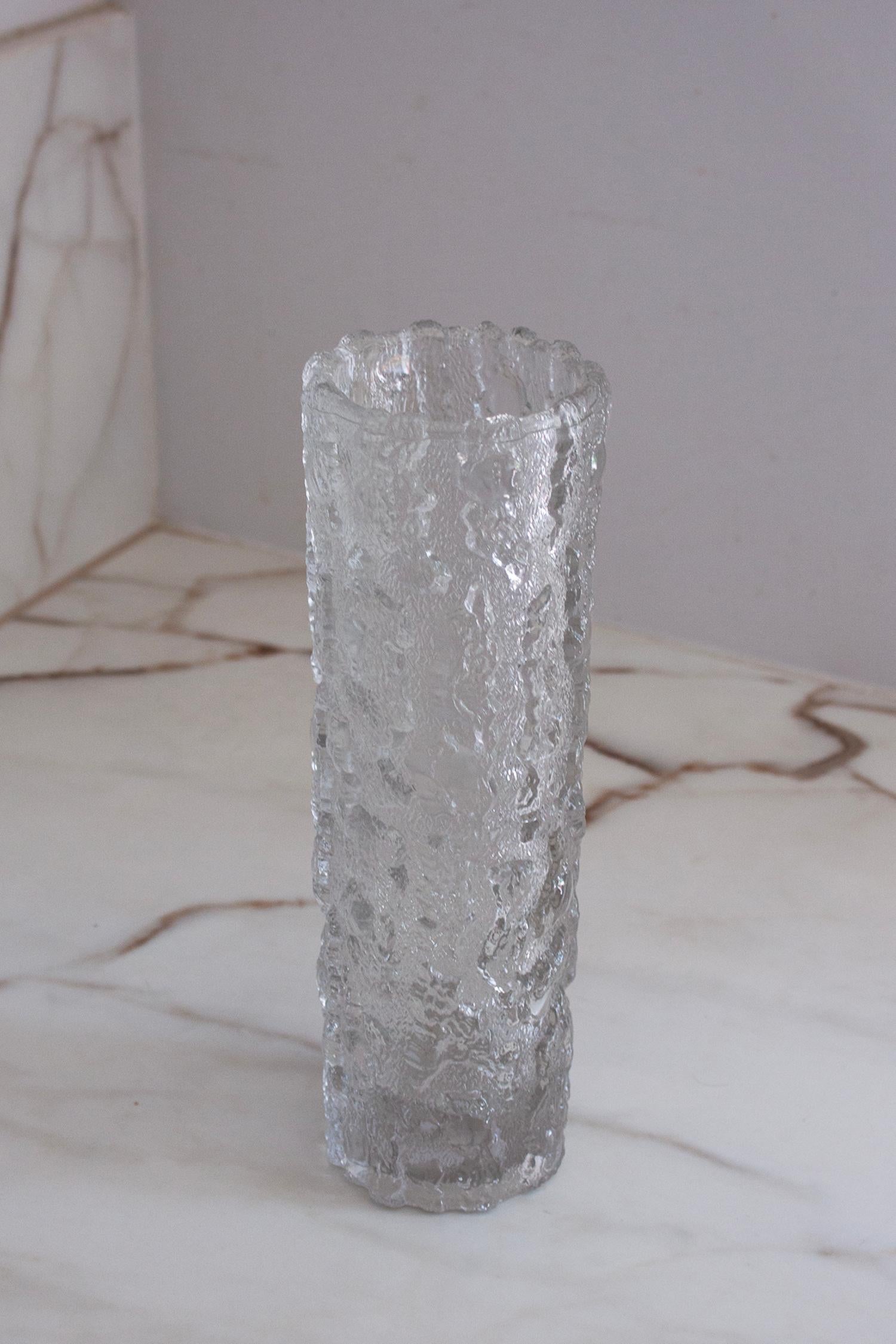 Ce grand vase en verre à glace mesure 27,5 cm de haut et 9 cm de diamètre. Il présente une surface texturée distinctive qui imite l'aspect de la glace craquelée. Ce style est devenu particulièrement populaire dans le design moderne du milieu du