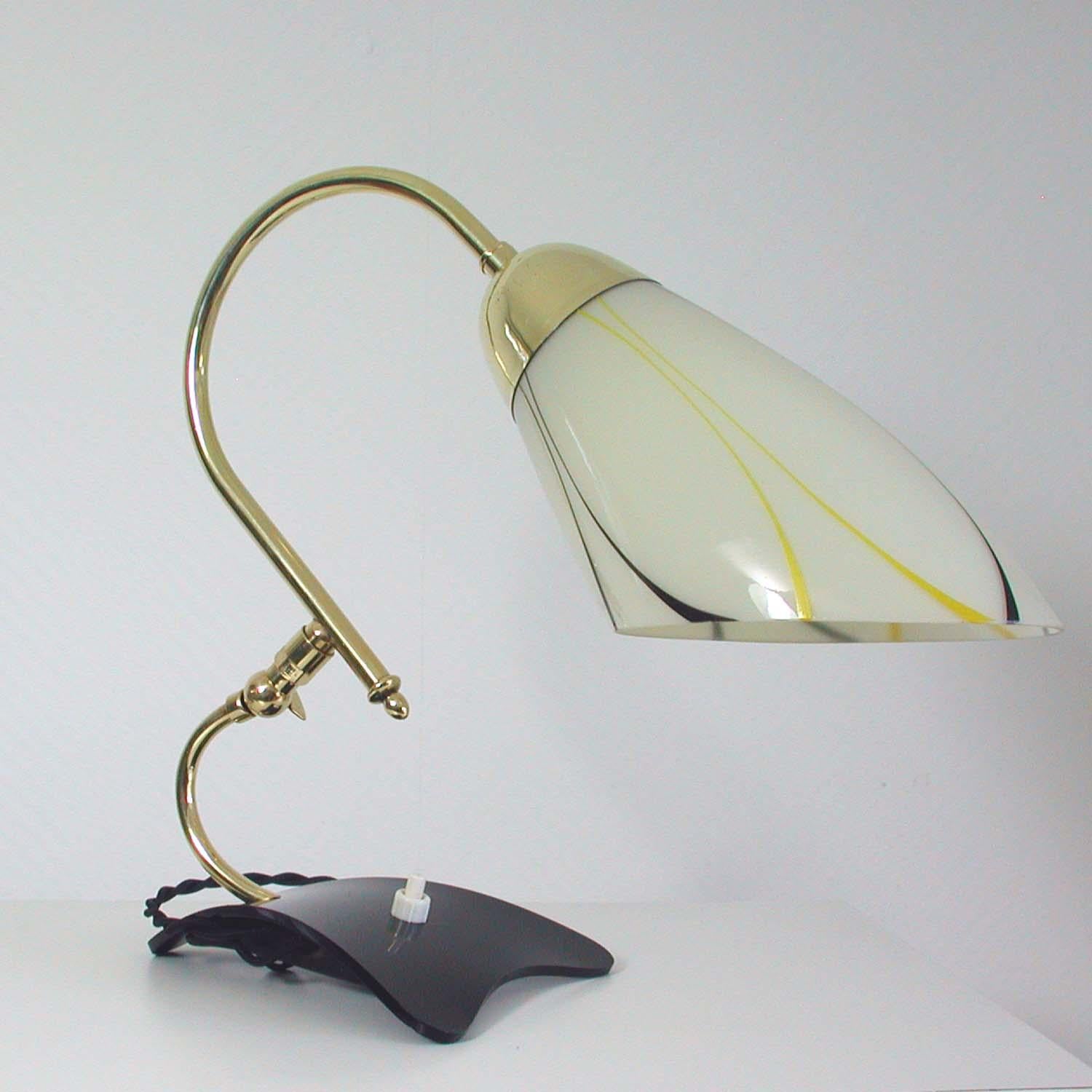 This beautiful table lamp was manufactured in Germany at the beginning of the 1950s.

It has got a black plastic base, an adjustable brass lamp arm and a yellow, white and black glass lampshade.

In excellent condition, rewired for North