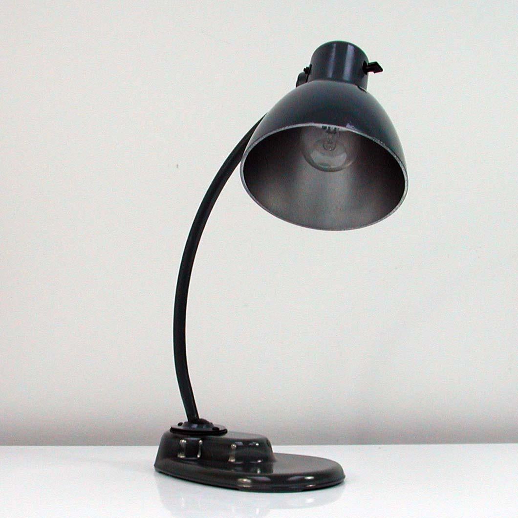 This model 1115 dark grey Bauhaus table lamp is based on an early design by Marianne Brandt for Kandem and features a glass foot as well as a lacquered bakelite shade. It was manufactured by Leuchtenbau Leipzig (formally Kandem) in 1951. The lamp
