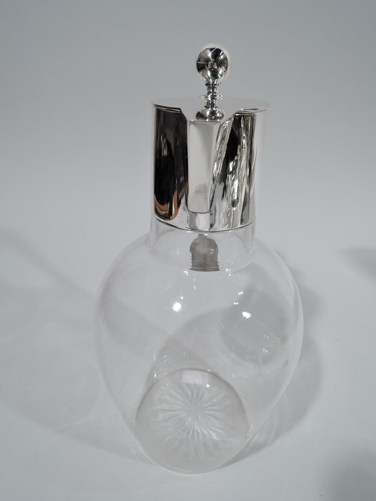 German Modern 800 silver and glass decanter, ca 1910. Ovoid glass body with star cut to underside. Drum-form neck and triangular spout. Cover flat and hinged with ball finial. Bracket handle. Silver fully marked including Koch & Bergfeld maker’s
