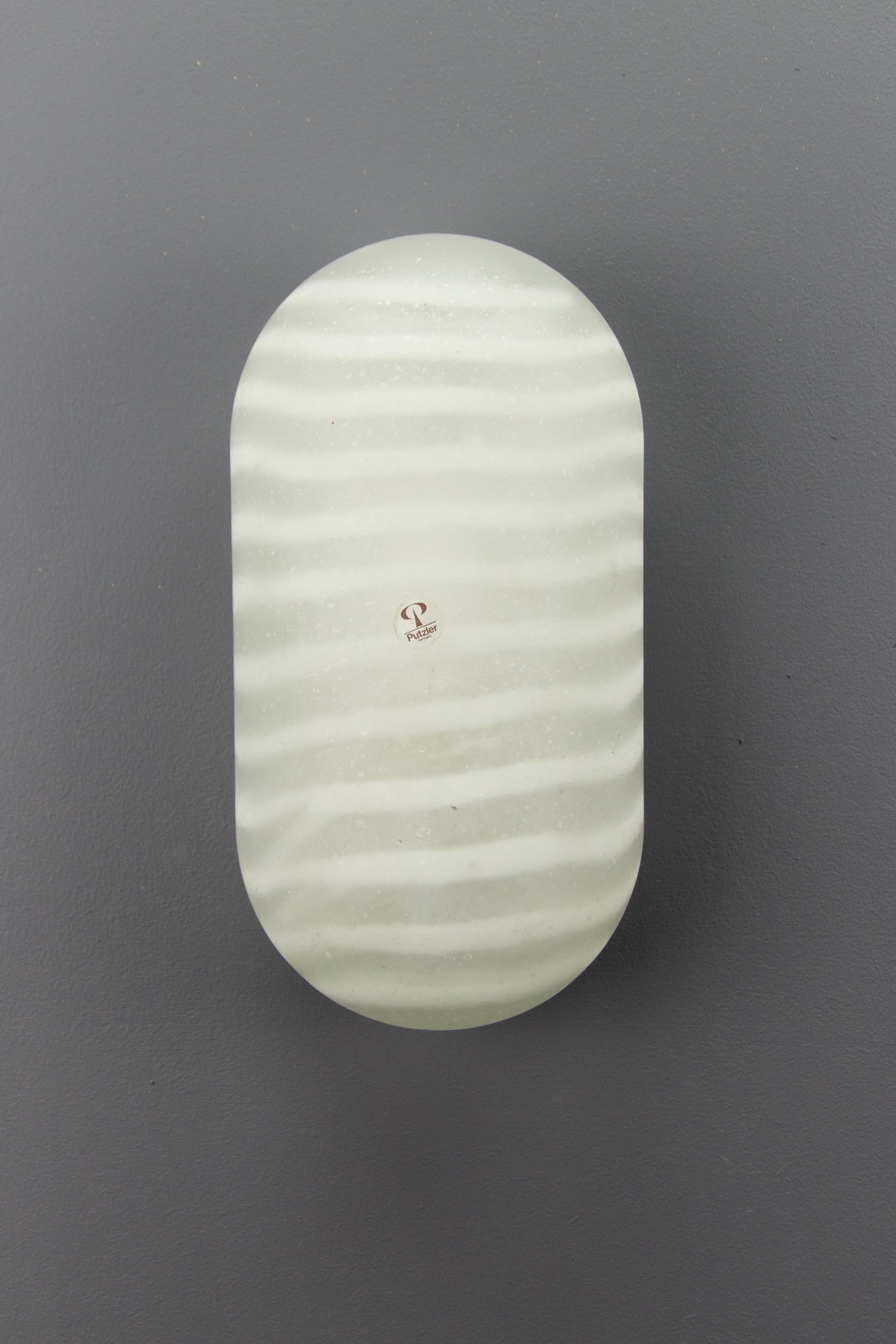 This adorable glass wall- or ceiling light made of thick hand-blown frosted glass features a design with darker and brighter stripes, manufactured by famous German glass manufacturer Peill & Putzler in the 1970s.
White color metal frame with one