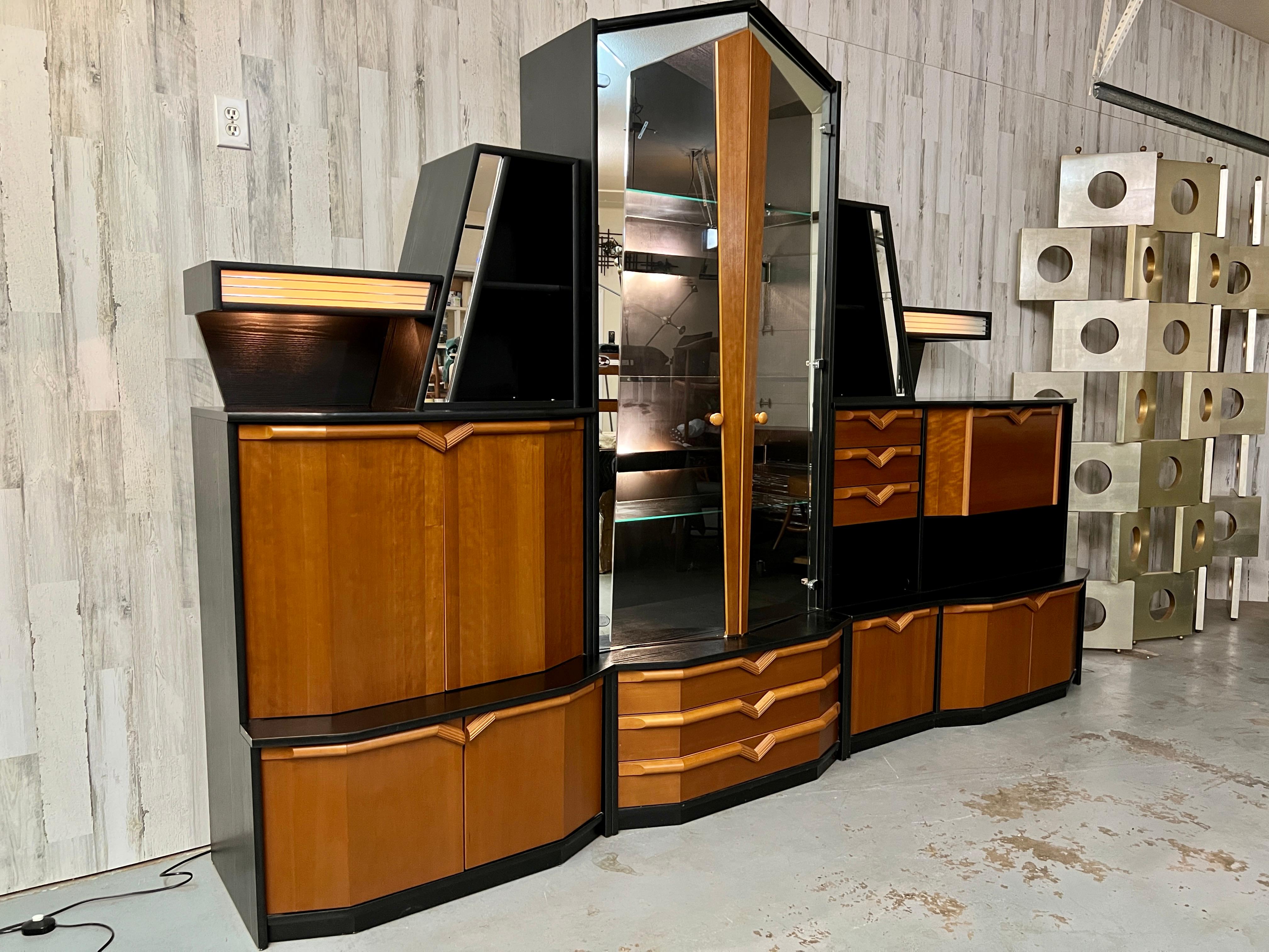 Combination of ebonized oak with teak and glass make this wall unit usable as a bookcase / display cabinet or media center. The faceted arched glass doors have mirrored borders with interior lights.
This unit comes in 3 sections, The display