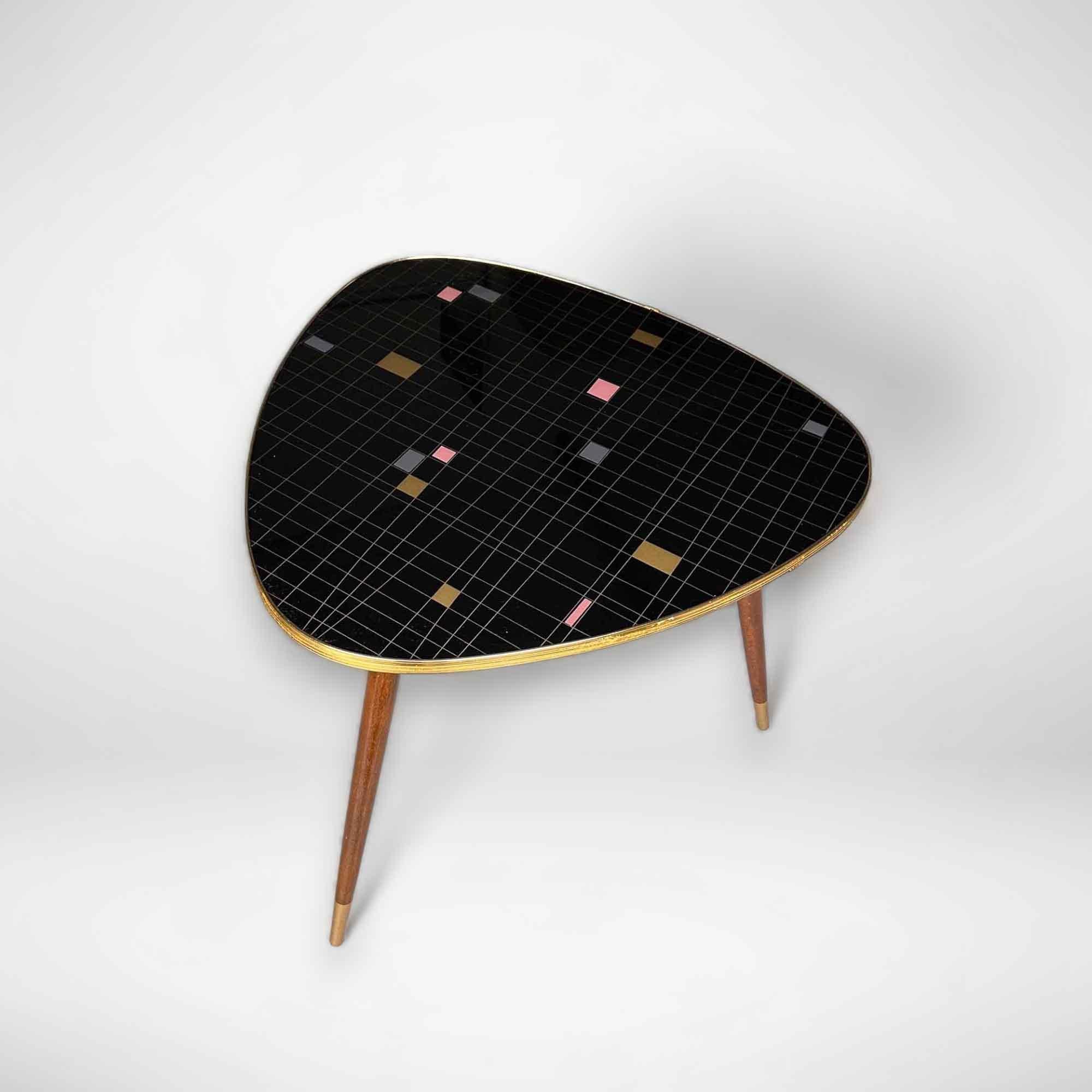 A beautiful fifties coffee table with an illustration in gold, gray, and pink on a black background. This vintage table has the typical gold edge and stands on 3 sturdy wooden legs. The style of this side table is also called 'rockabilly', 'atomic