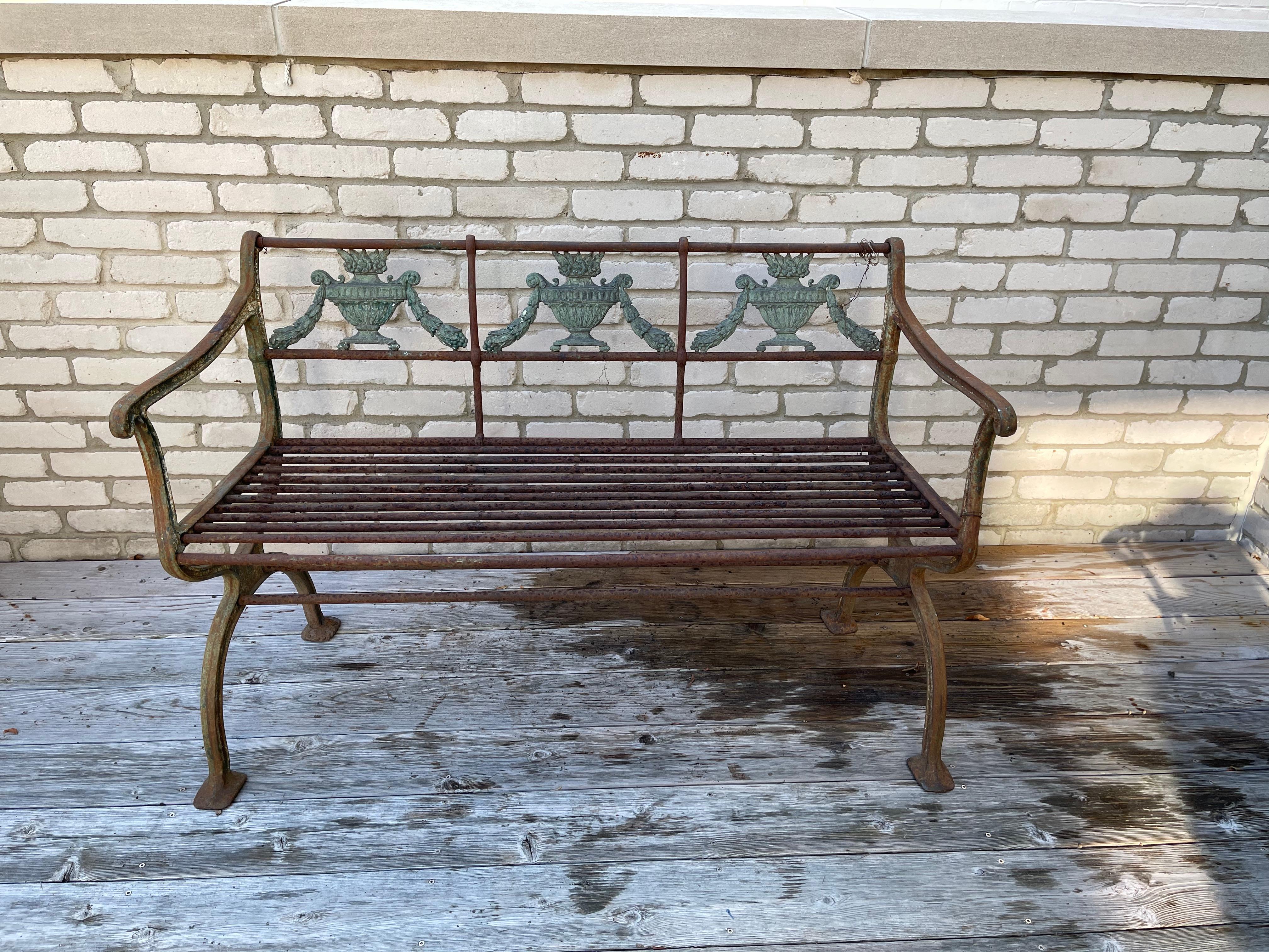 German neoclassical painted green cast iron garden set consisting of bench and two arm chairs. The backs inset with floral-filled classical urn flanked by festooning, downswept arms raised on c-scroll terminals connected with grilled rod seat