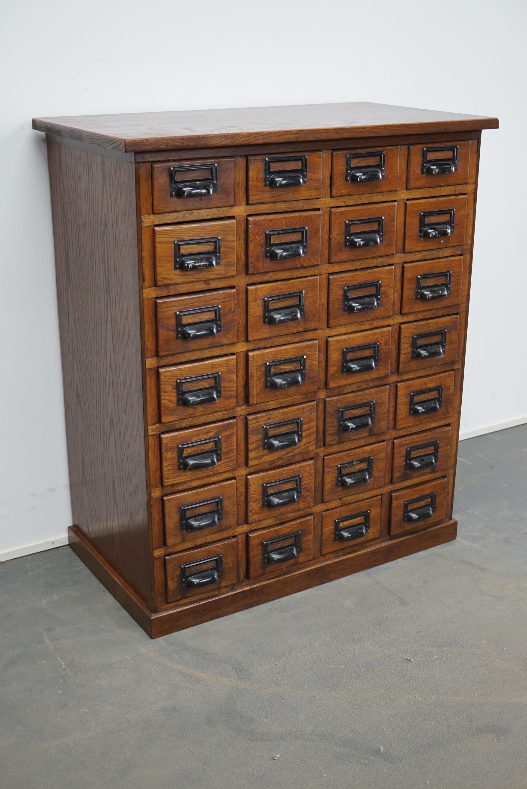 This apothecary cabinet was made circa 1930s in Germany. It features 28 drawers with nice black metal handles. It is made oak and it remains in a very good condition.