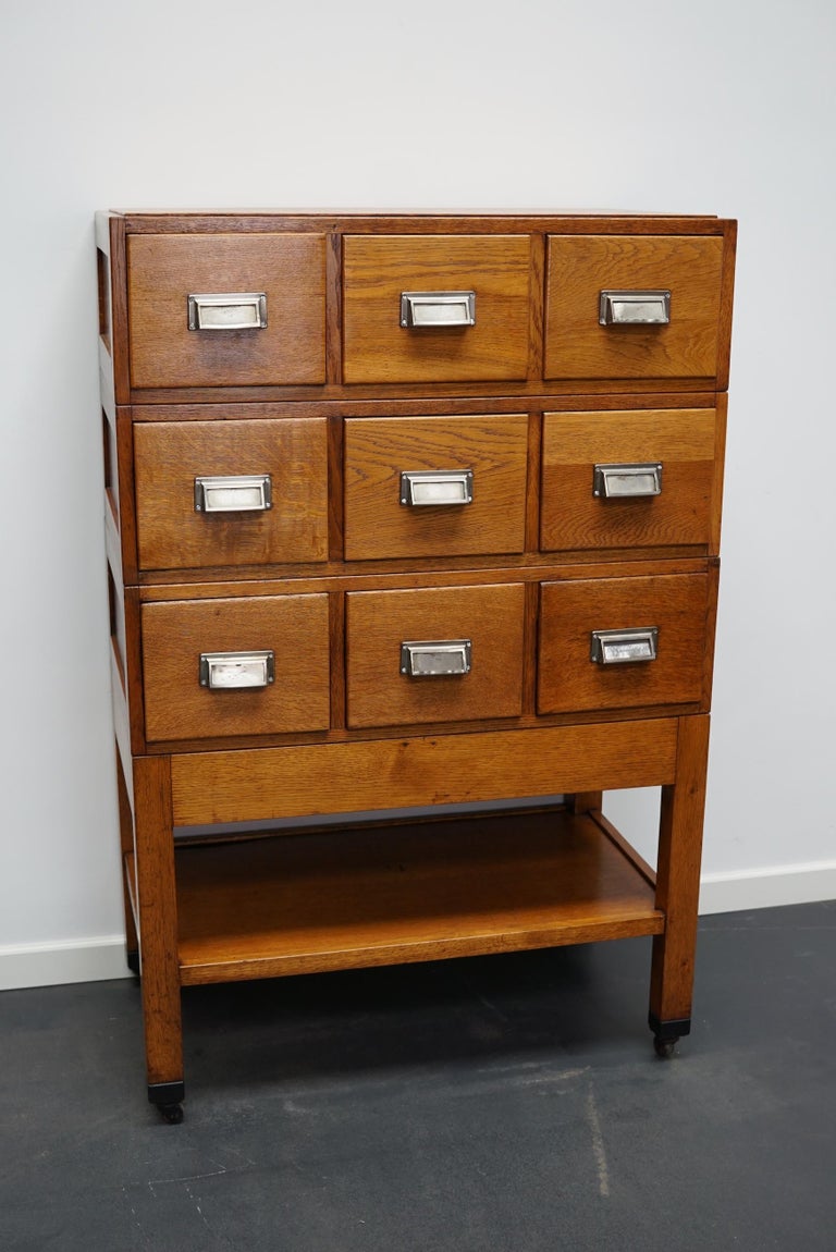 This apothecary cabinet was made from oak circa 1950s in Germany. It features 9 drawers with metal cup handles and a shelve at the bottom. The interior dimensions of the drawers are: D x W x H: 39 x 21 x 15.5 / 10 cm.