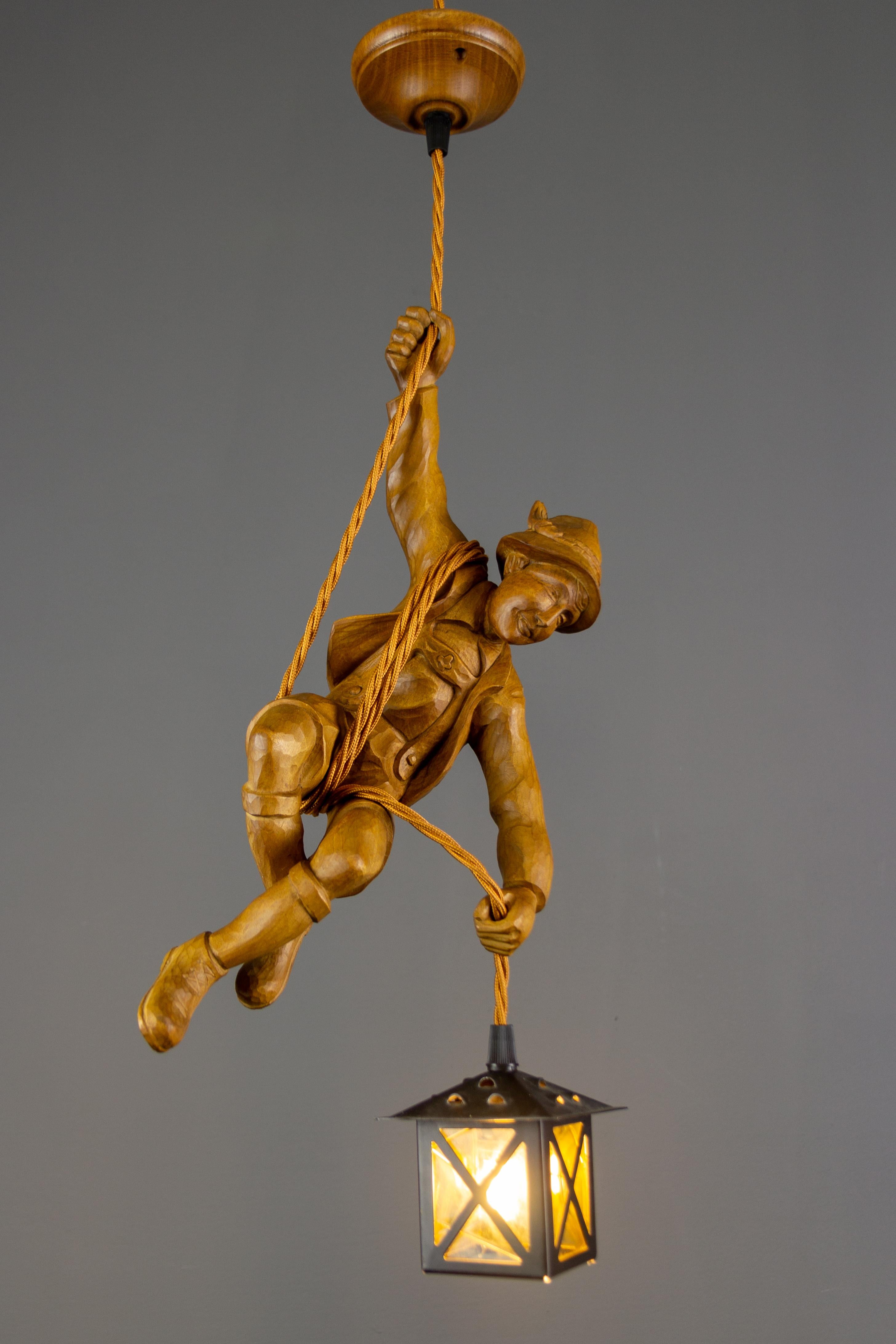 Wonderful German figural pendant lamp features a hand carved figure of a smiling mountain climber. The detailed carved wooden mountaineer is holding onto a rope and holding metal and yellow glass lantern in one hand.
The height of the pendant lamp