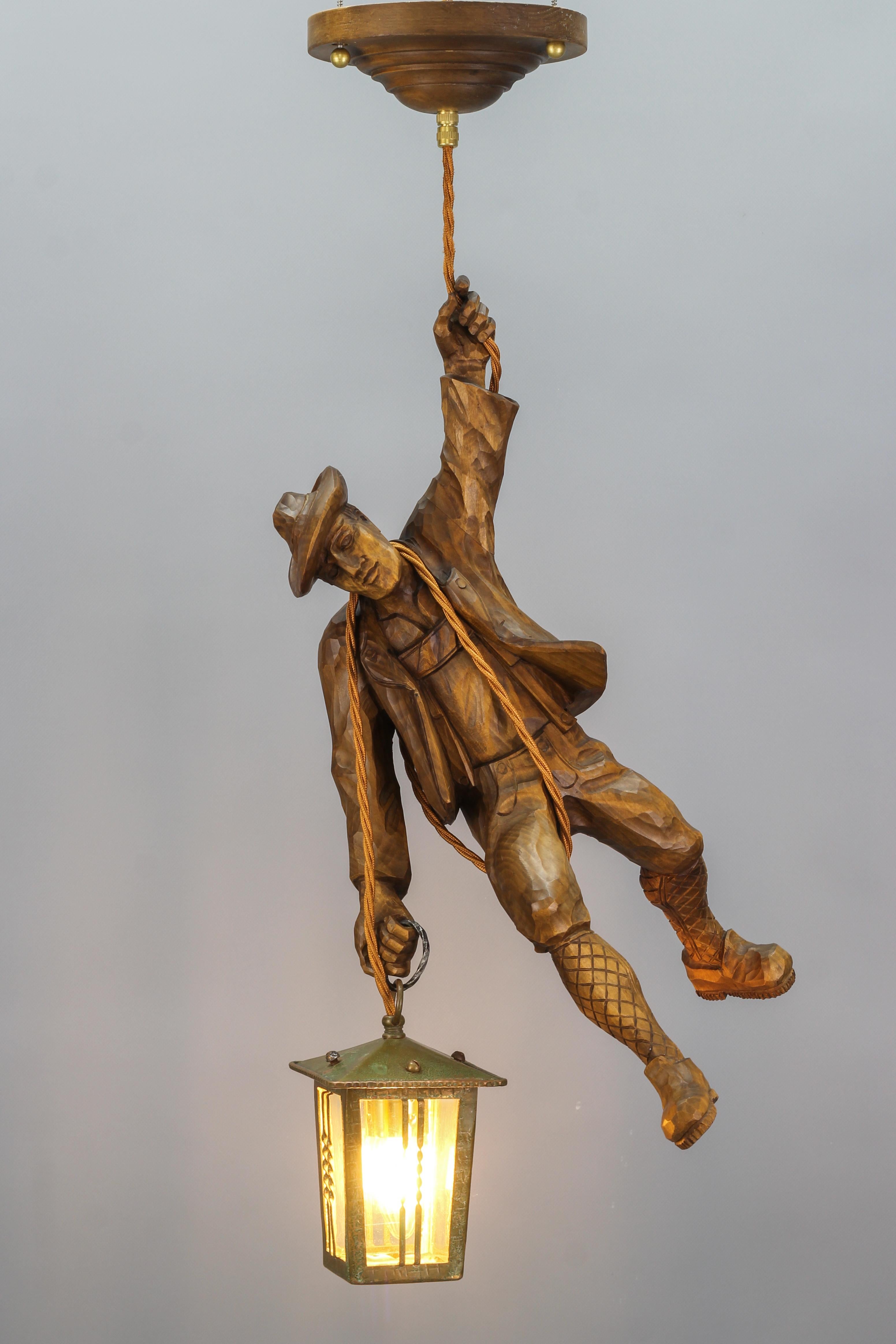 Cette magnifique lampe suspendue figurative allemande présente une grande figure en bois de tilleul sculptée à la main représentant un alpiniste. L'alpiniste en bois sculpté se tient à une corde et tient une lanterne dans une main. La figurine est