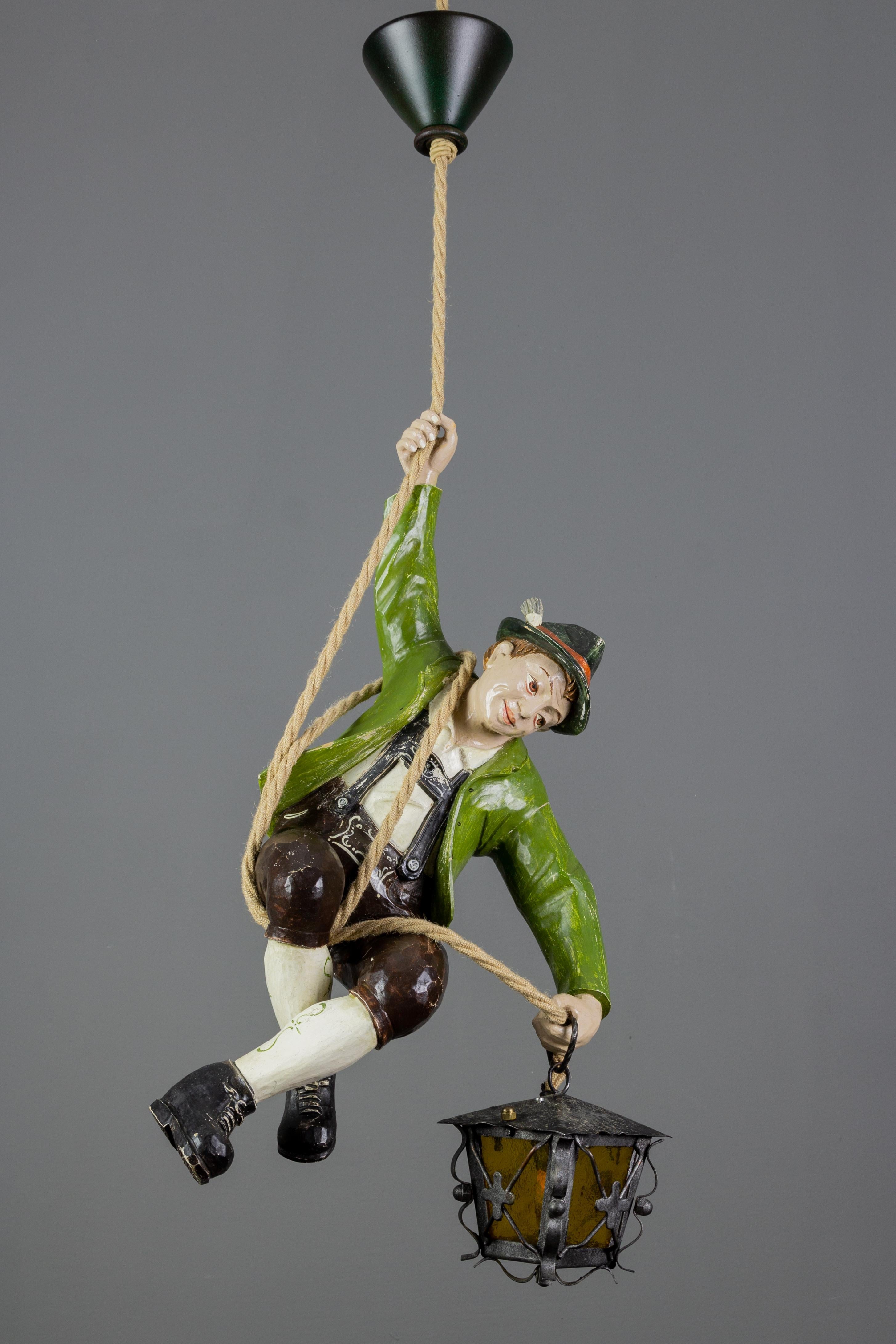 The wonderful German pendant light features a hand-carved figure of a mountain climber in beautifully hand-painted Bavarian traditional clothing in green, black, white, and red colors. The detailed carved wooden mountaineer wears a hat and is
