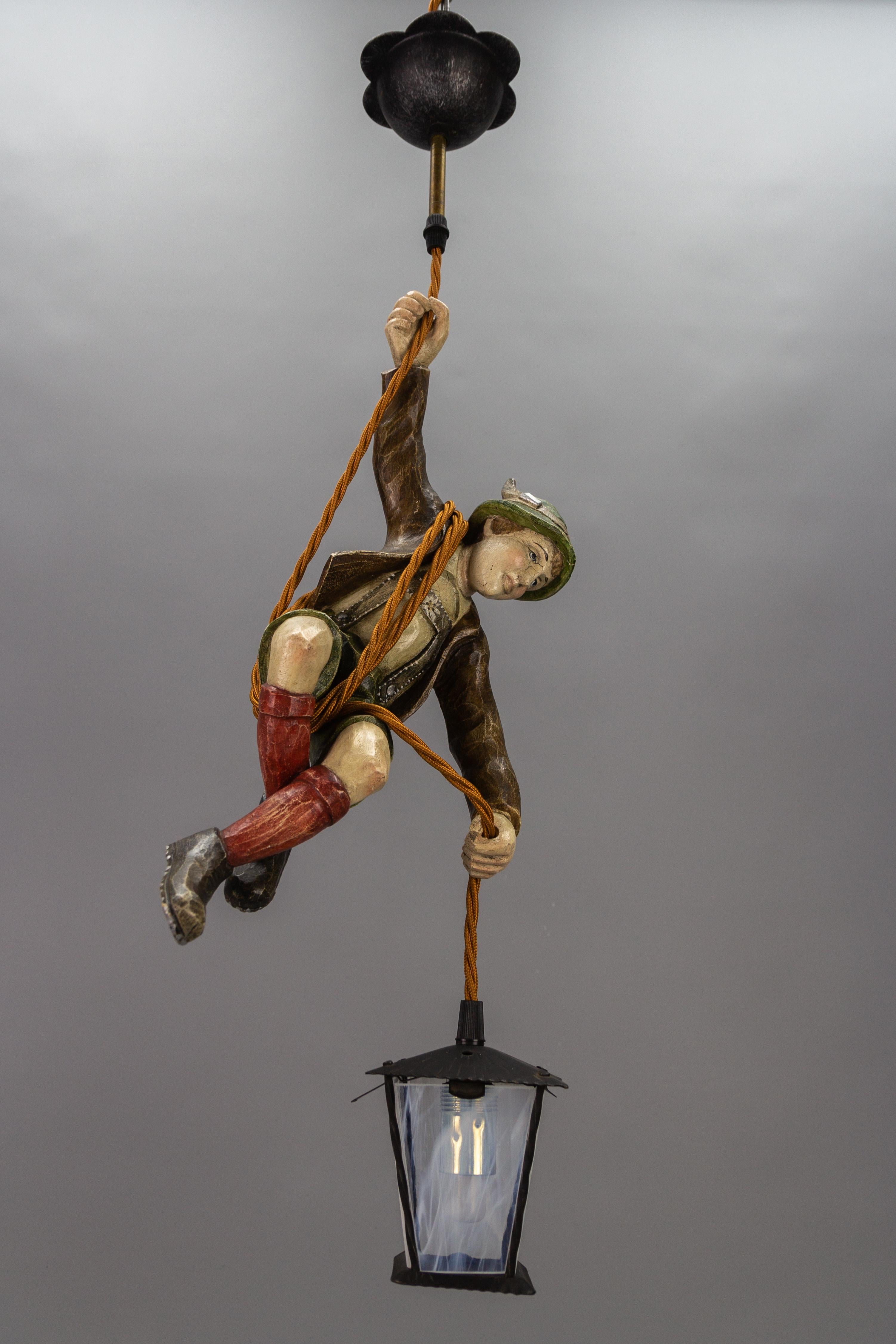 Cette magnifique lampe suspendue allemande ou Lüstermännchen représente un alpiniste sculpté à la main et portant de magnifiques vêtements traditionnels bavarois peints à la main dans des couleurs marron, vert, blanc et rouge. L'alpiniste en bois