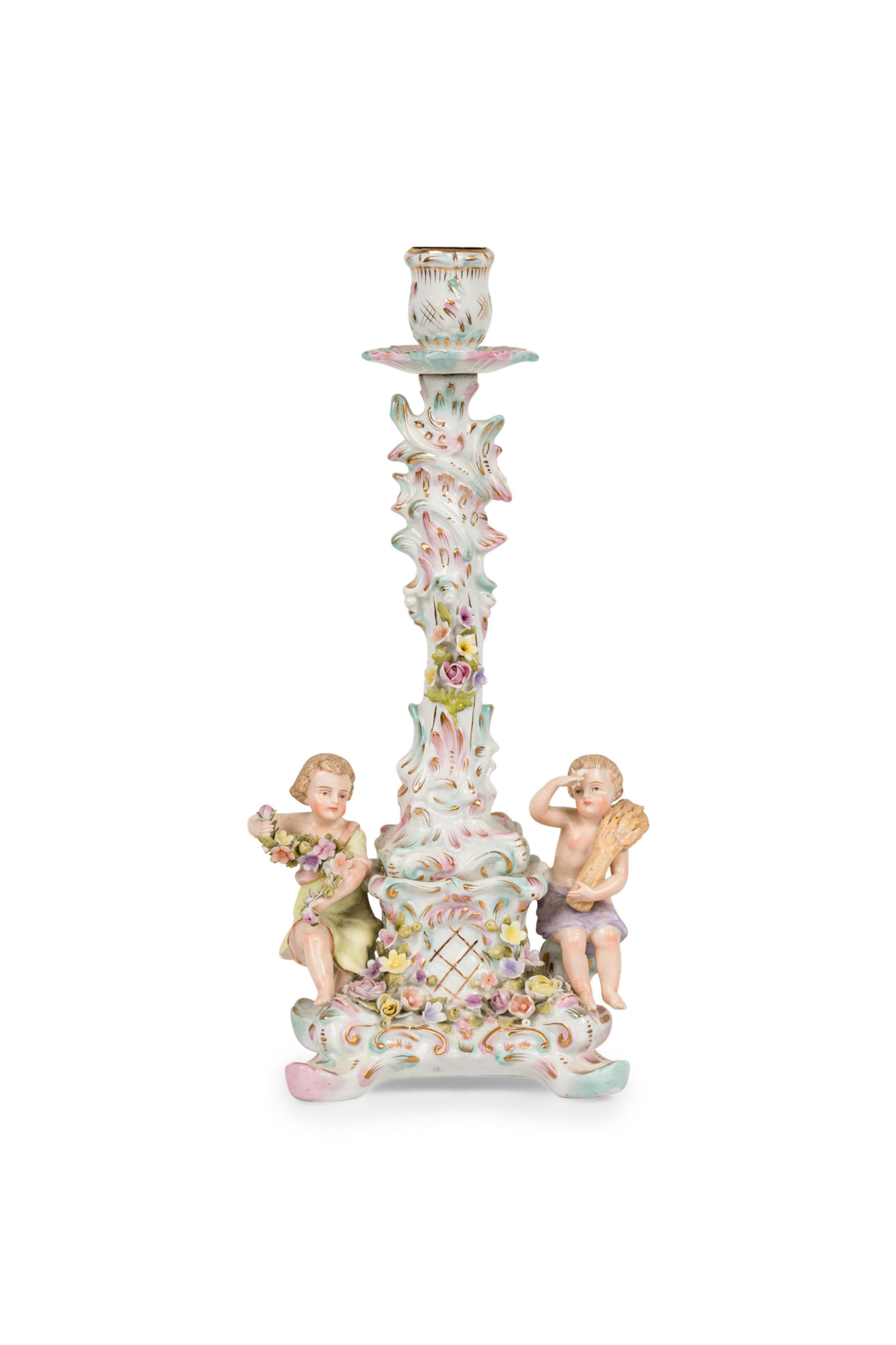 German Meissen style (19th Century) porcelain candlestick of a male and female putti figures sitting on opposite sides of a square shaped base holding flowers and a branch