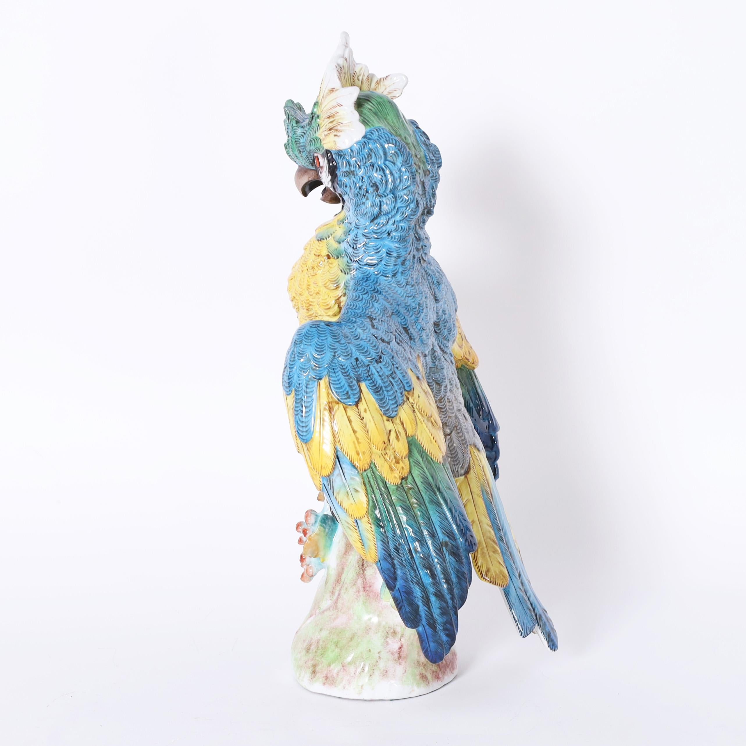 Standout life size porcelain parrot hand decorated in vivid tropical colors, glazed and perched on a tree trunk. Signed with crossed arrows on the back.