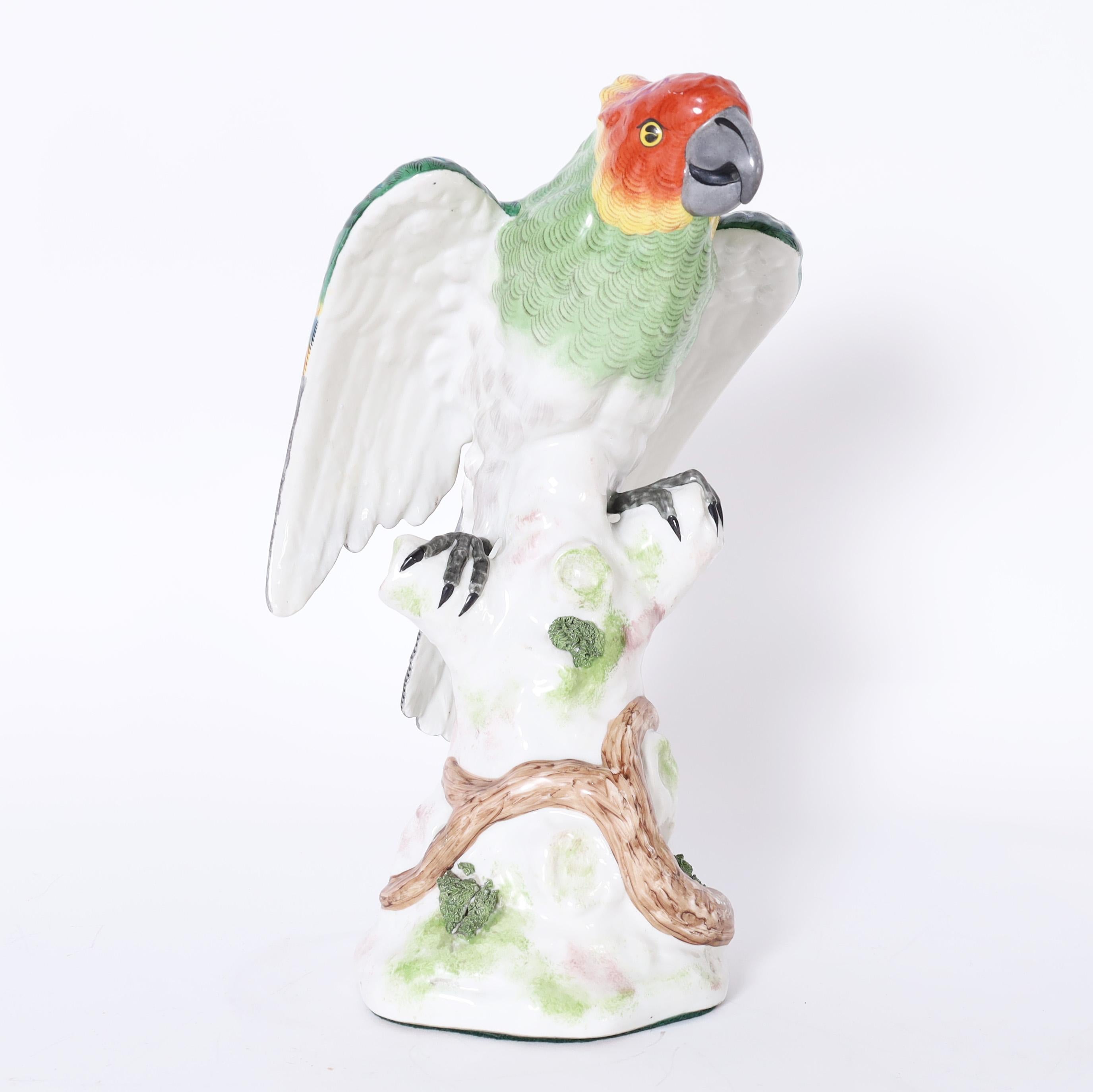Charming life size porcelain parrot hand decorated in vivid tropical colors, glazed and perched on a tree trunk. Signed with crossed arrows on the back.