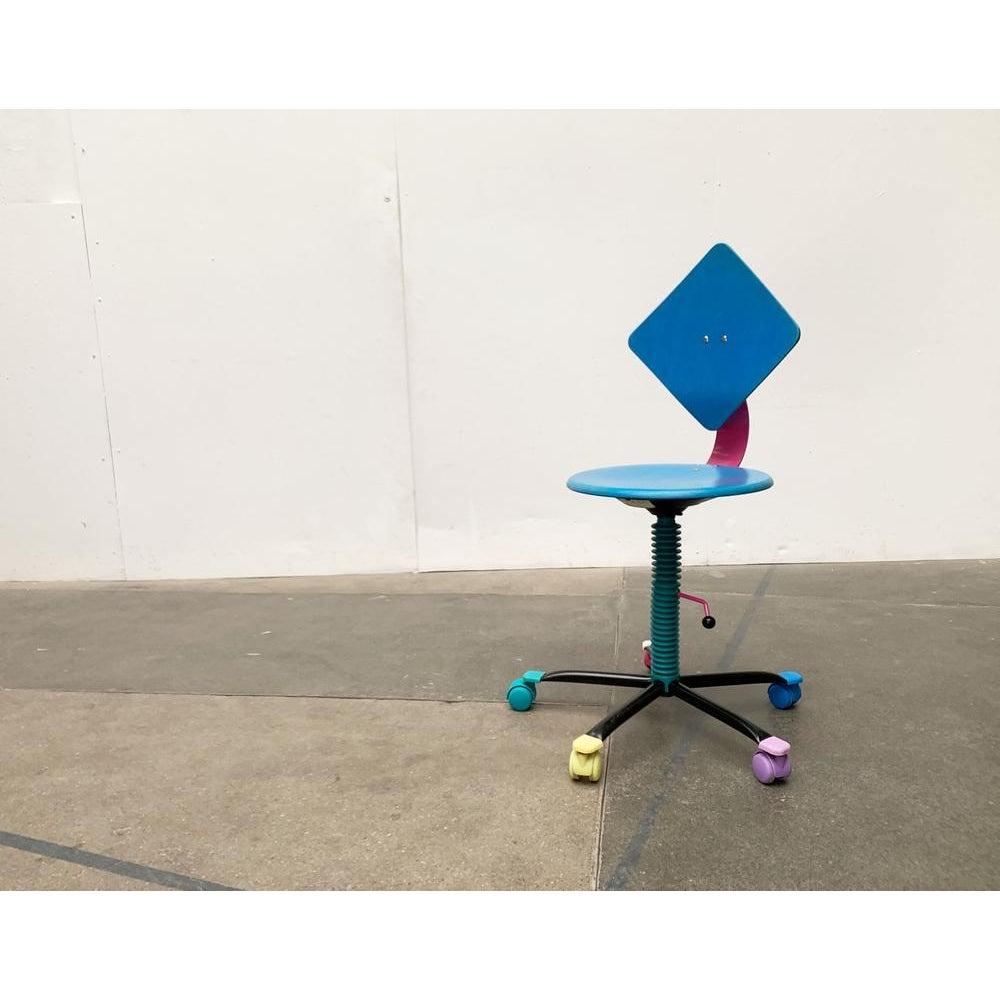 Chaise de bureau postmoderne du fabricant allemand impac datant du début des années 90.

un design fortement marqué par un langage de conception et un univers de couleurs postmodernes. L'assise et le dossier sont en bois et laqués. Le dossier est