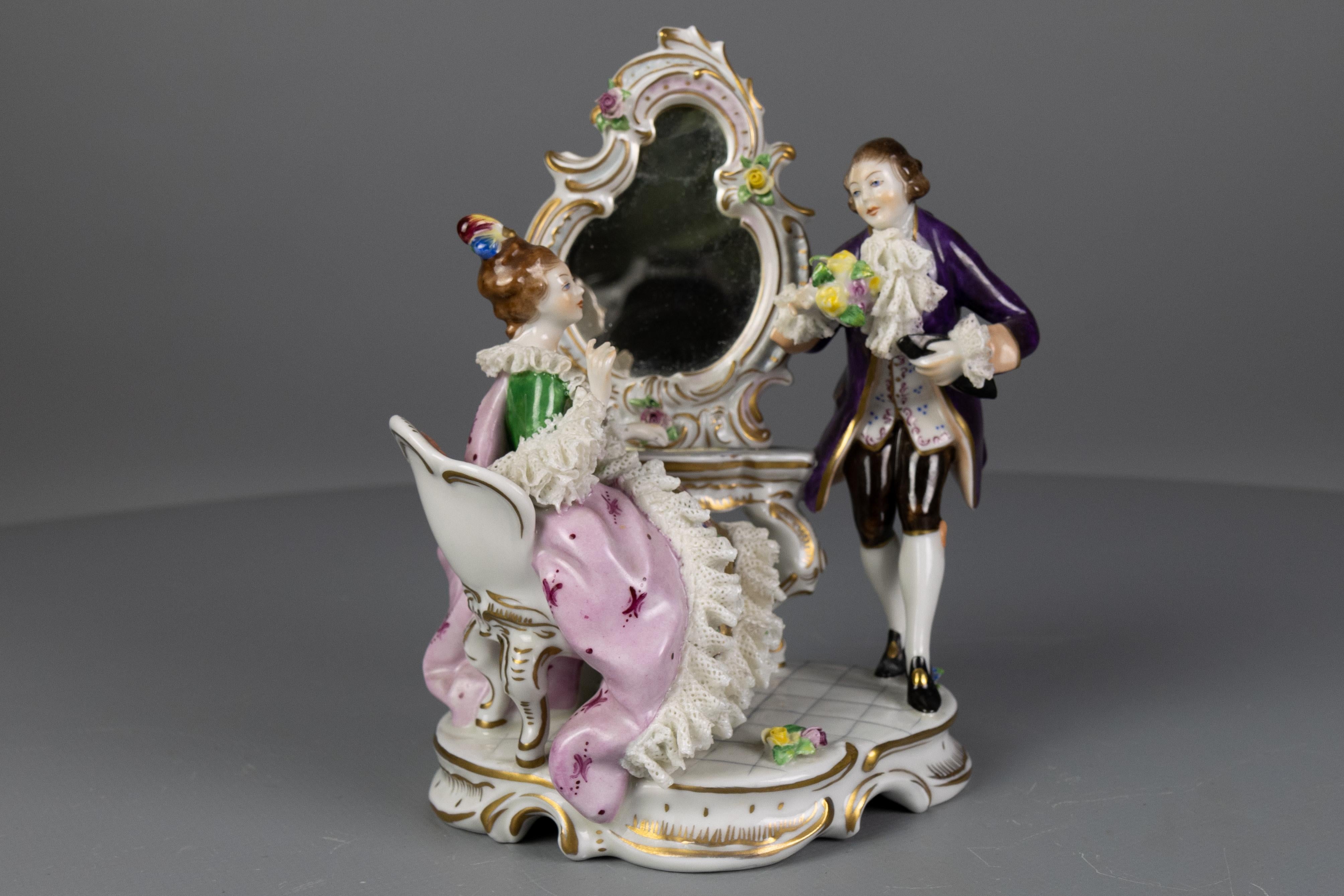 Deutsche Rokoko-Porzellanfigur eines Paares am Frisiertisch, ca. 1950er Jahre, Älteste Volkstedter Porzellanmanufaktur.
Diese bezaubernde Porzellanfigurengruppe zeigt ein Paar in Rokoko-Kleidung und Rokoko-Möbeln: Die Dame sitzt auf einem Stuhl an