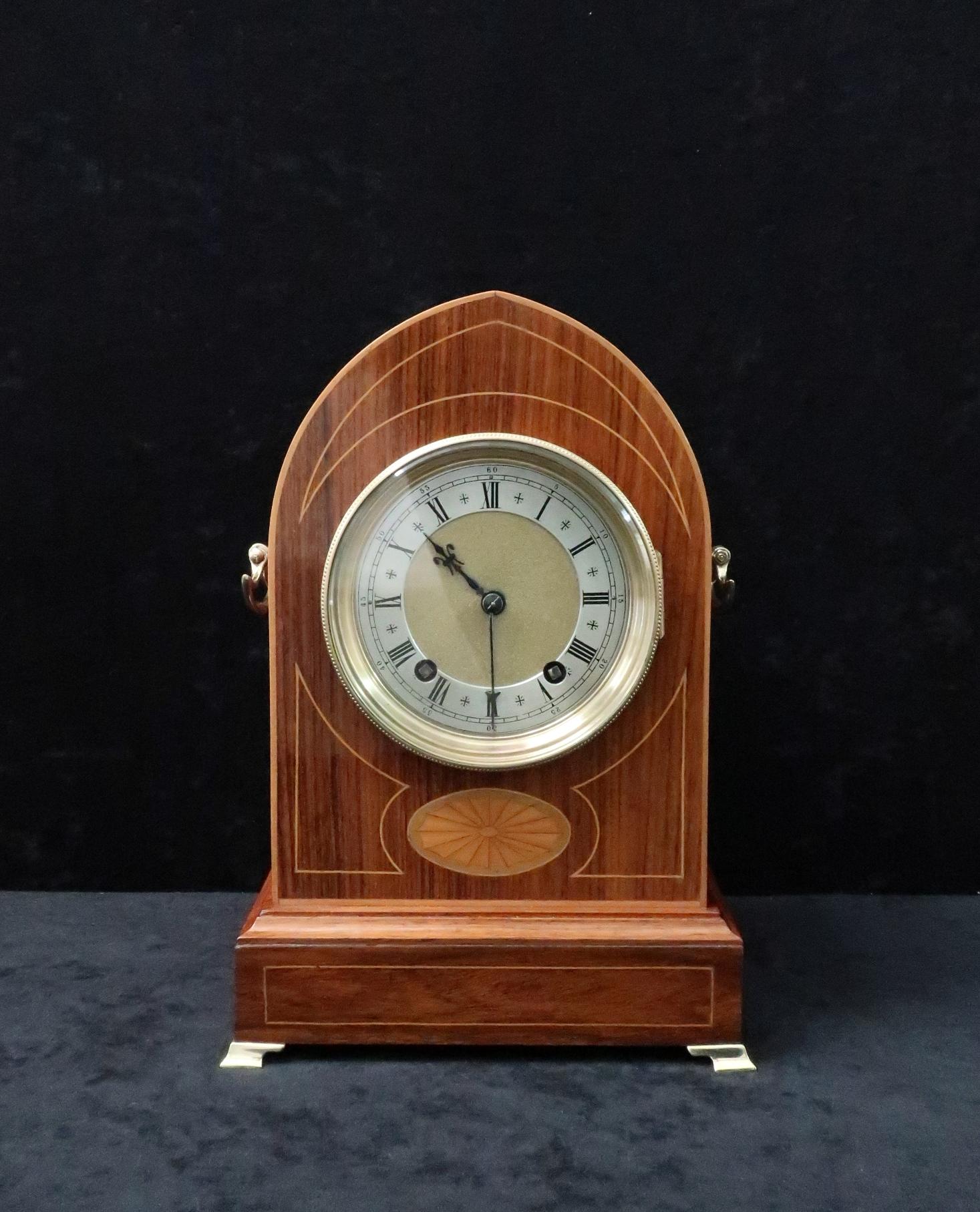 A very good quality German figured rosewood lancet shaped mantel clock with boxwood stringing and fan inlay to the front of the case and brass carrying handles to the sides. The clock has a brass dial with silvered chapter ring and an eight day