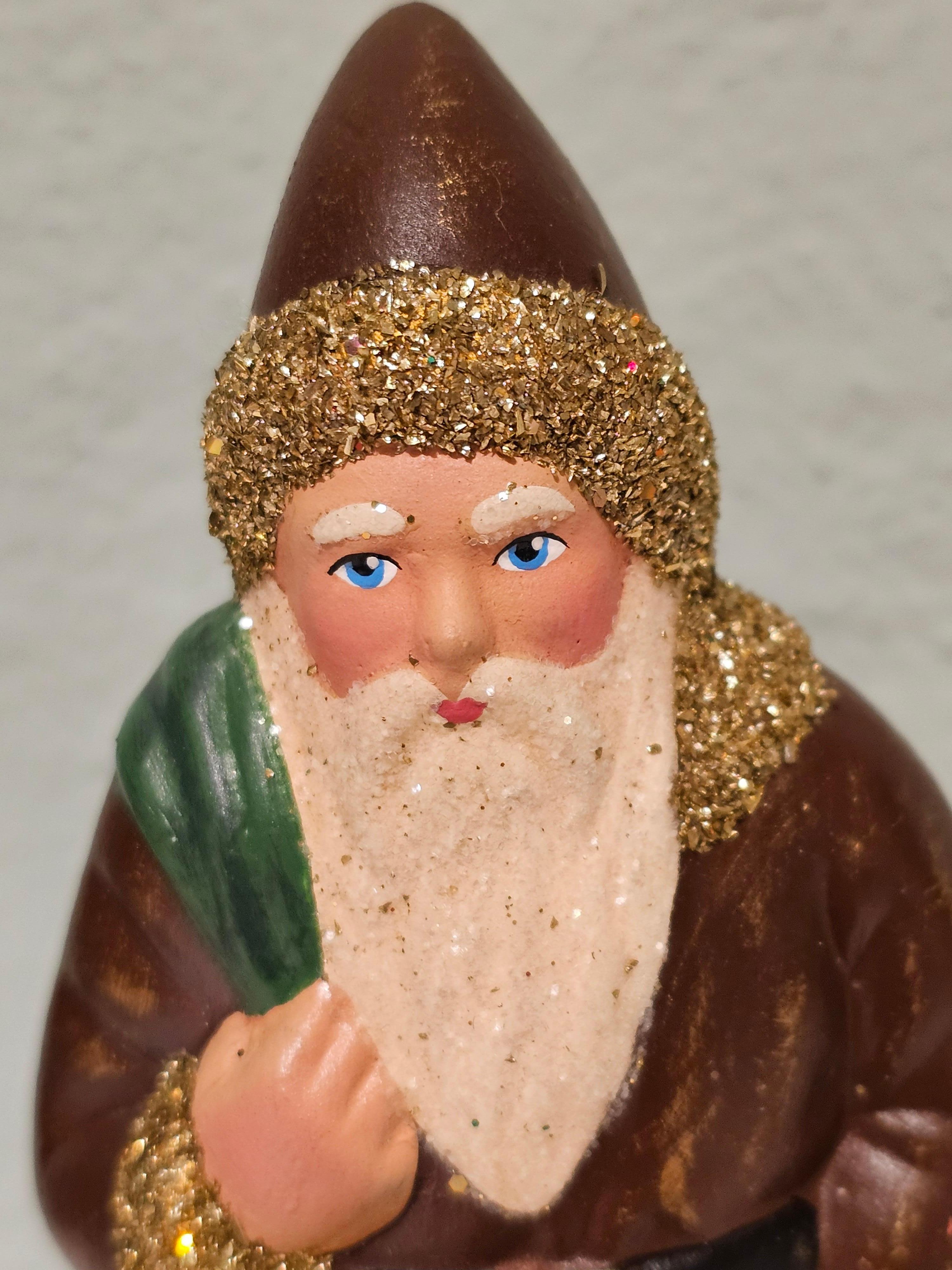 Deutsche Weihnachtsmannfigur aus Pappmaché mit handbemaltem, detailliertem Gesicht. Sie hält einen Nikolaussack und ist mit goldenen Glitzerdetails verziert.
Der Weihnachtsmann wird in der originalen antiken Form in Deutschland handgefertigt.