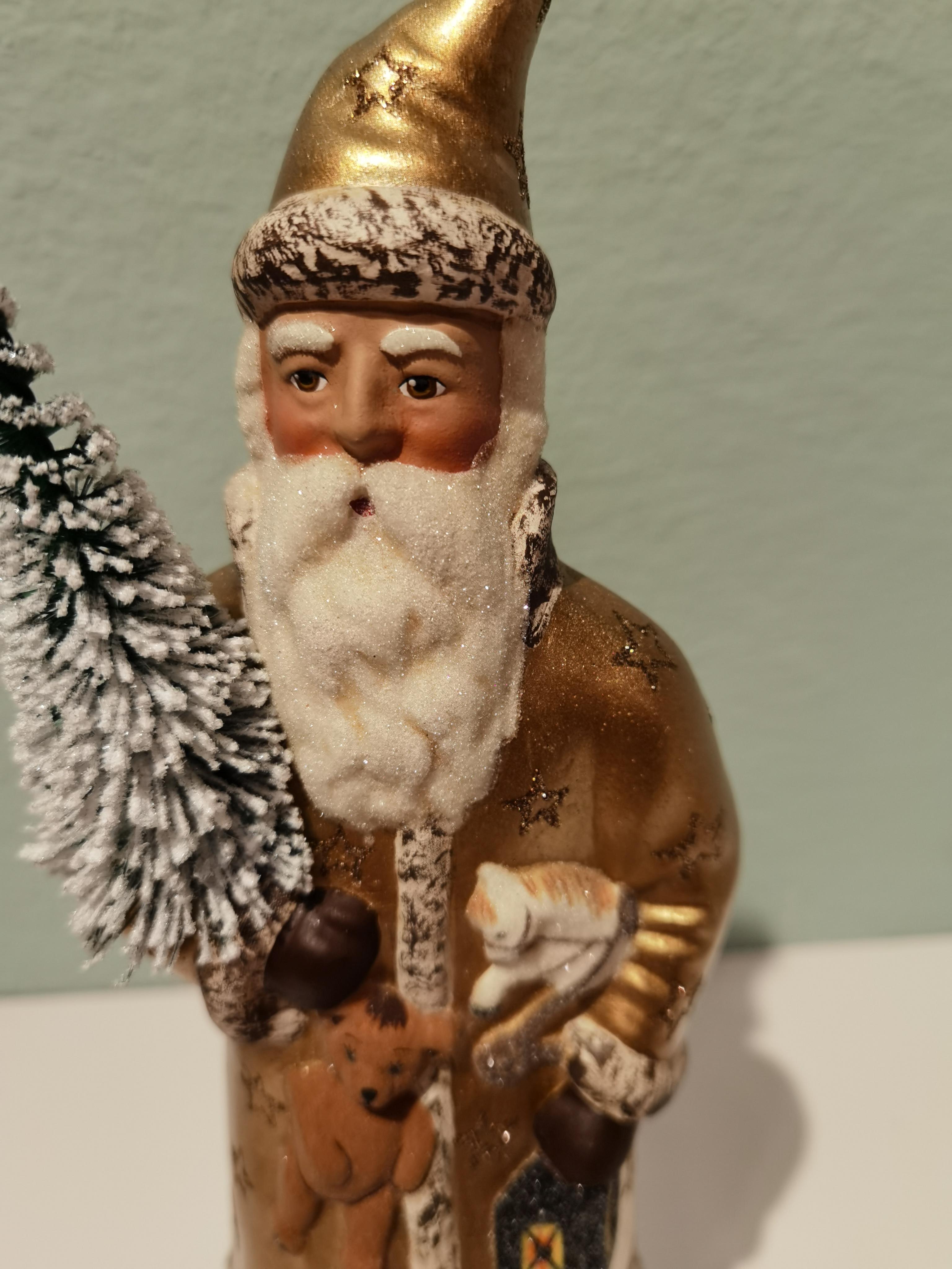 Santa Claus figure in hand painted gold papier mâché decorated with stars and a hand painted detailed face holding a tree. The Santa Claus is handmade in a original antique mould in Germany.