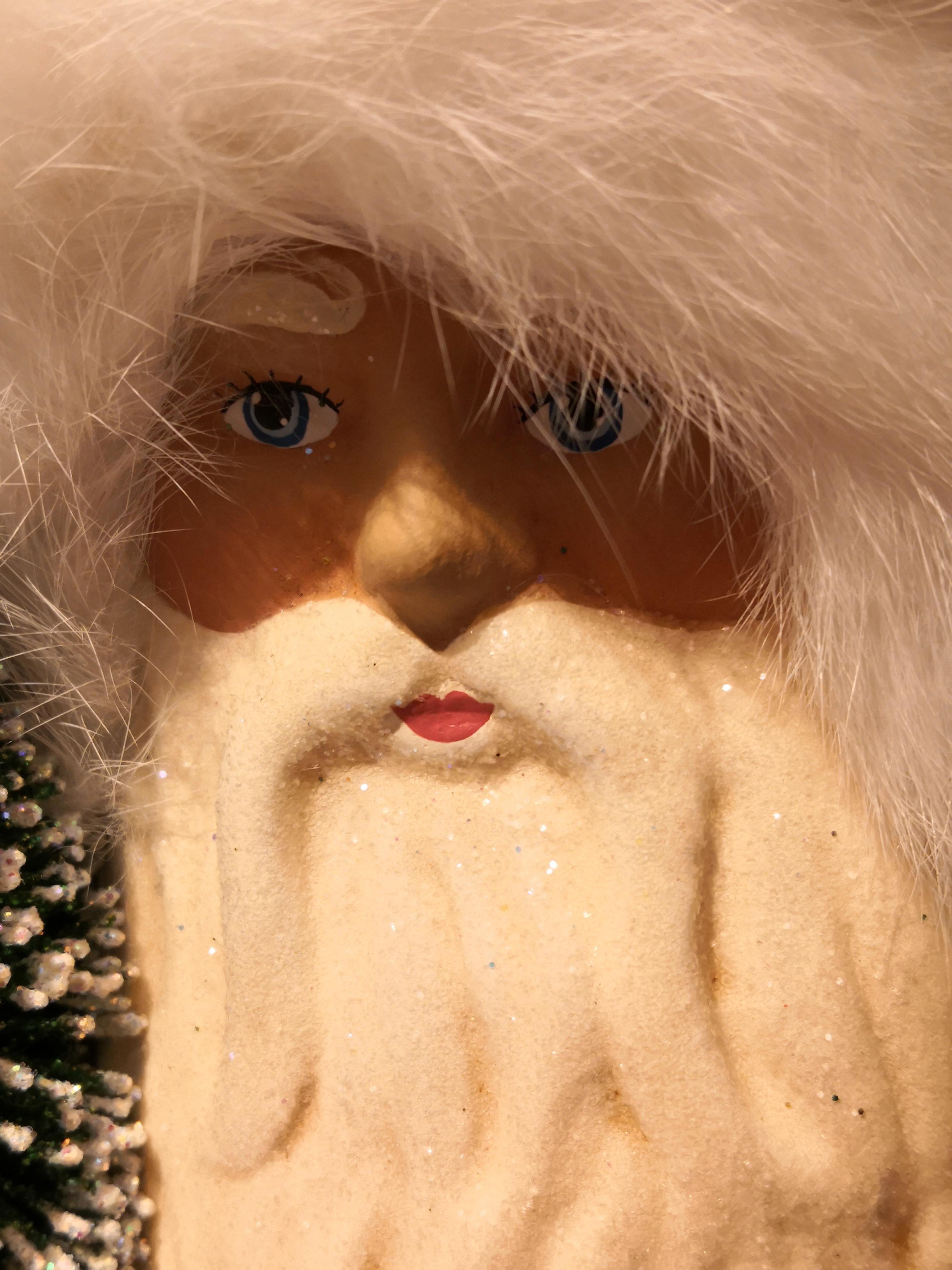Große Weihnachtsmannfigur aus Pappmaché mit handbemaltem, detailliertem Gesicht. Sie hält einen Baum und ist mit Glitzerdetails und einem echten Fellrand verziert.
Der Weihnachtsmann wird in der originalen antiken Form in Deutschland handgefertigt.