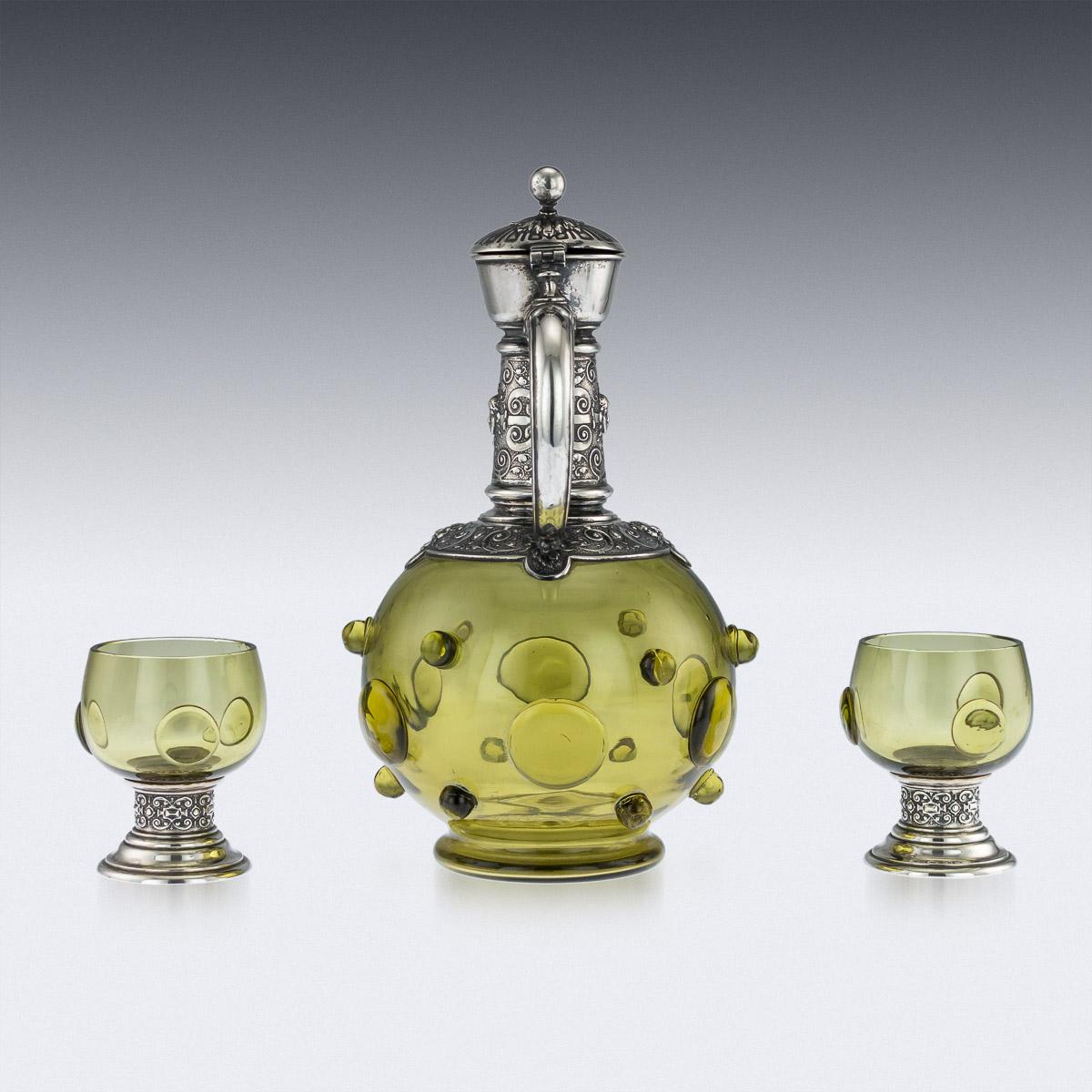 Antique late 19th century German solid silver and green glass decorative wine claret jug and pair of goblets, bulbous green glass body applied with unusual ball decoration, the silver mount is chased with Cellini inspired classical motifs, C-shaped