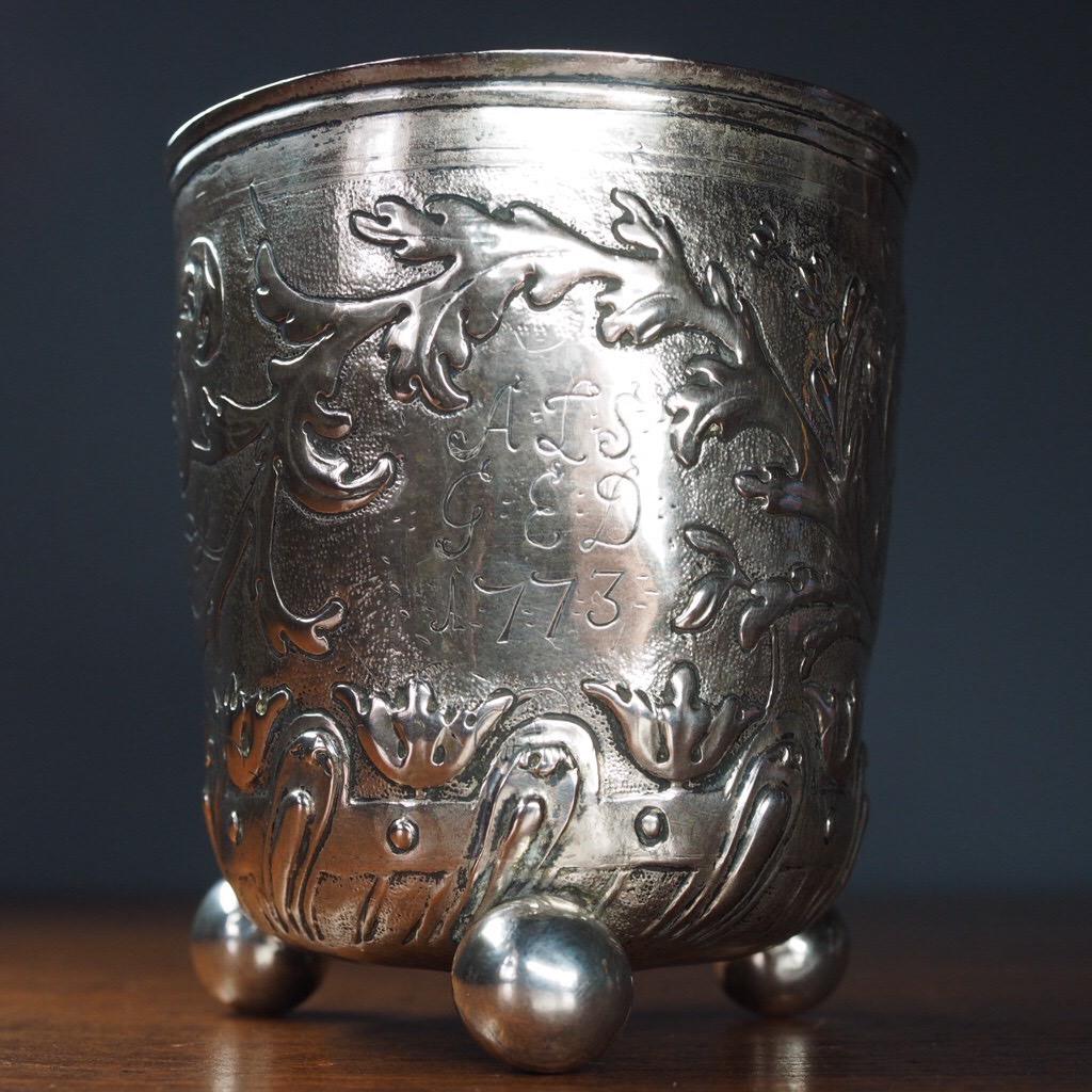 Remarkable German Baroque silver beaker, the cylindrical body embossed with a frieze of scrollwork, a complex gadrooned border to the rounded base including flowerheads and strapwork, resting on three ball feet.
Unmarked, circa 1710.
  