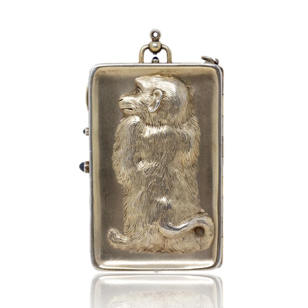 The minaudière of rectangular form with curved corners features a repousse monkey which humorously goes through the case with the front side of the monkey on the cover and the rear side of the monkey on the back. The exterior of the case is gilded
