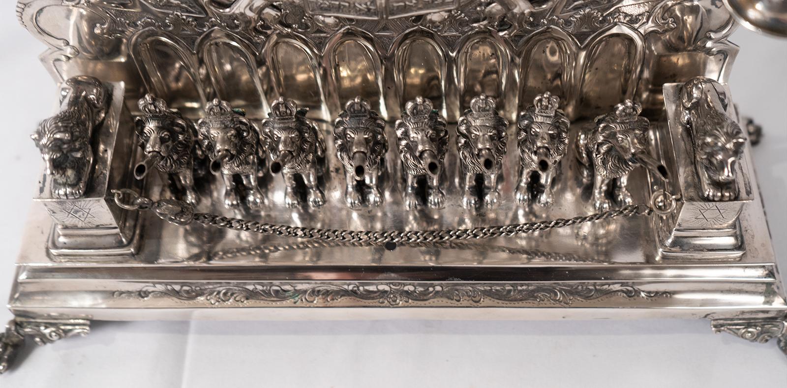 German silver Hanukkah lamp Menorah with gold washed lions: Approx. 50.21 Troy ounces .800 Silver. Surmounting Crown over a scrolling foliate and floral medallion design, with Ten Commandments, flanked by lions with crowns. Two Lion's head pitchers