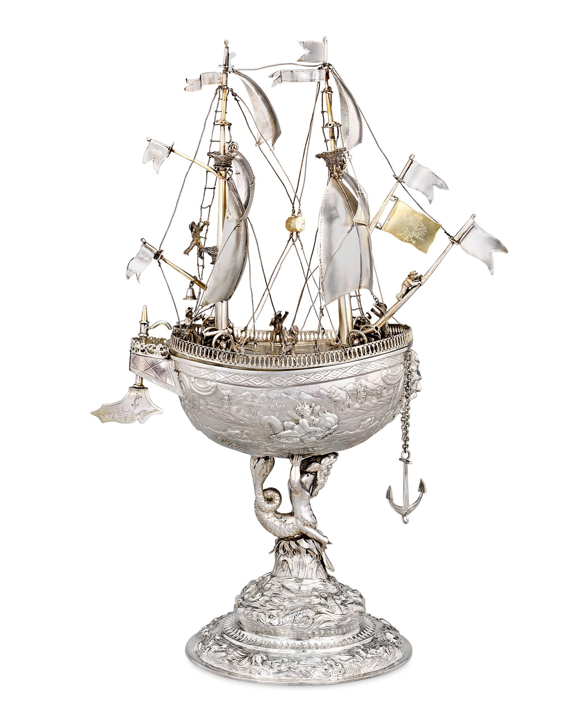This colossal silver nef is a spectacular example of German silverwork from the town of Hanau. The stunning vessel is covered with incredible detailing and decoration. This silver and parcel-gilt objet d’art, with its billowing sails, flags and a