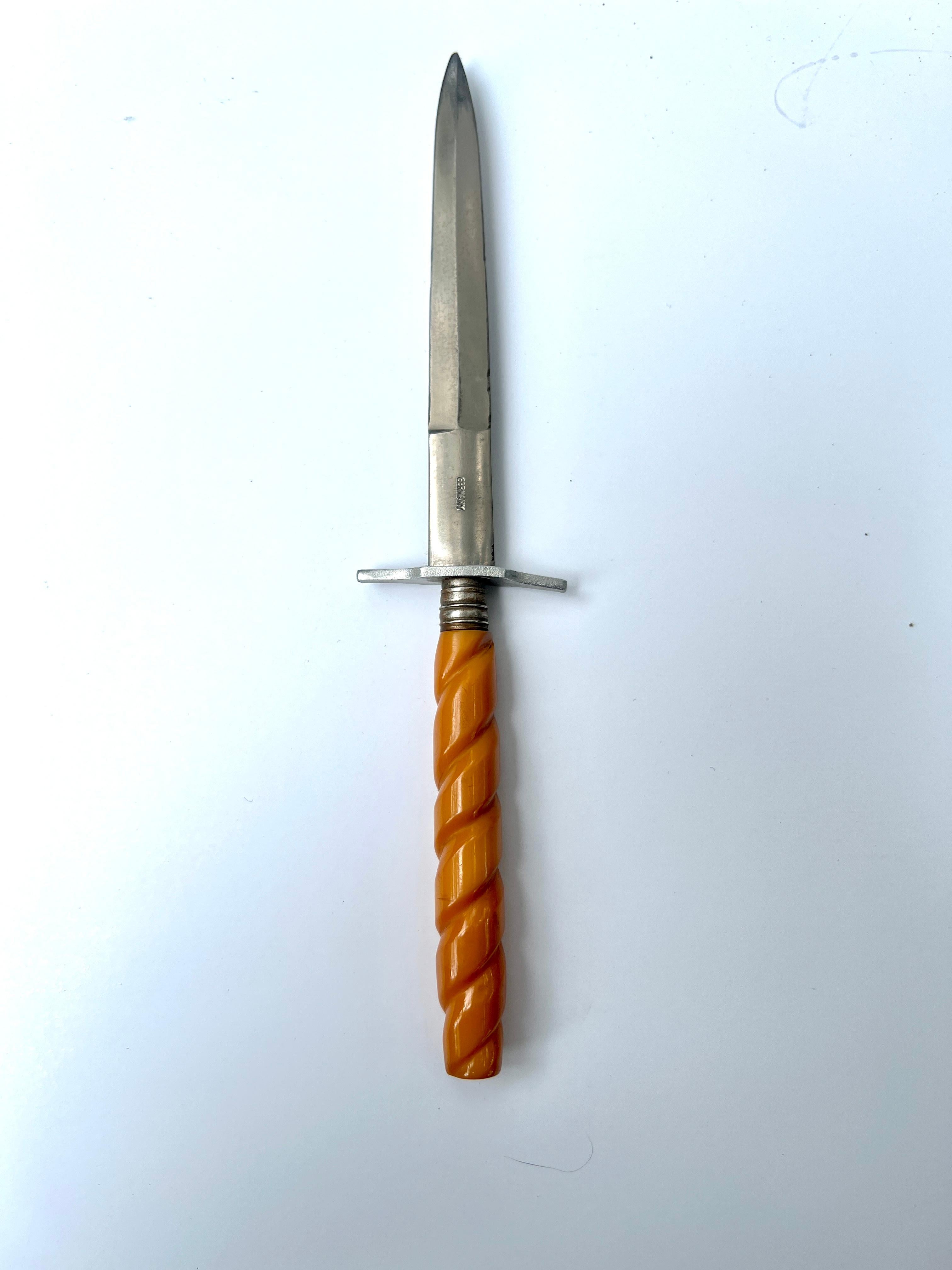 Ein schöner Brieföffner aus deutschem Stahl mit einem einzigartigen kaki-farbenen Bakelit-Griff mit Wirbel.

Ein Kompliment für jeden Schreibtisch oder Arbeitsplatz - schön auf einem mit interessanten Stiften gefüllten Zylinder ausgestellt.

Bitte
