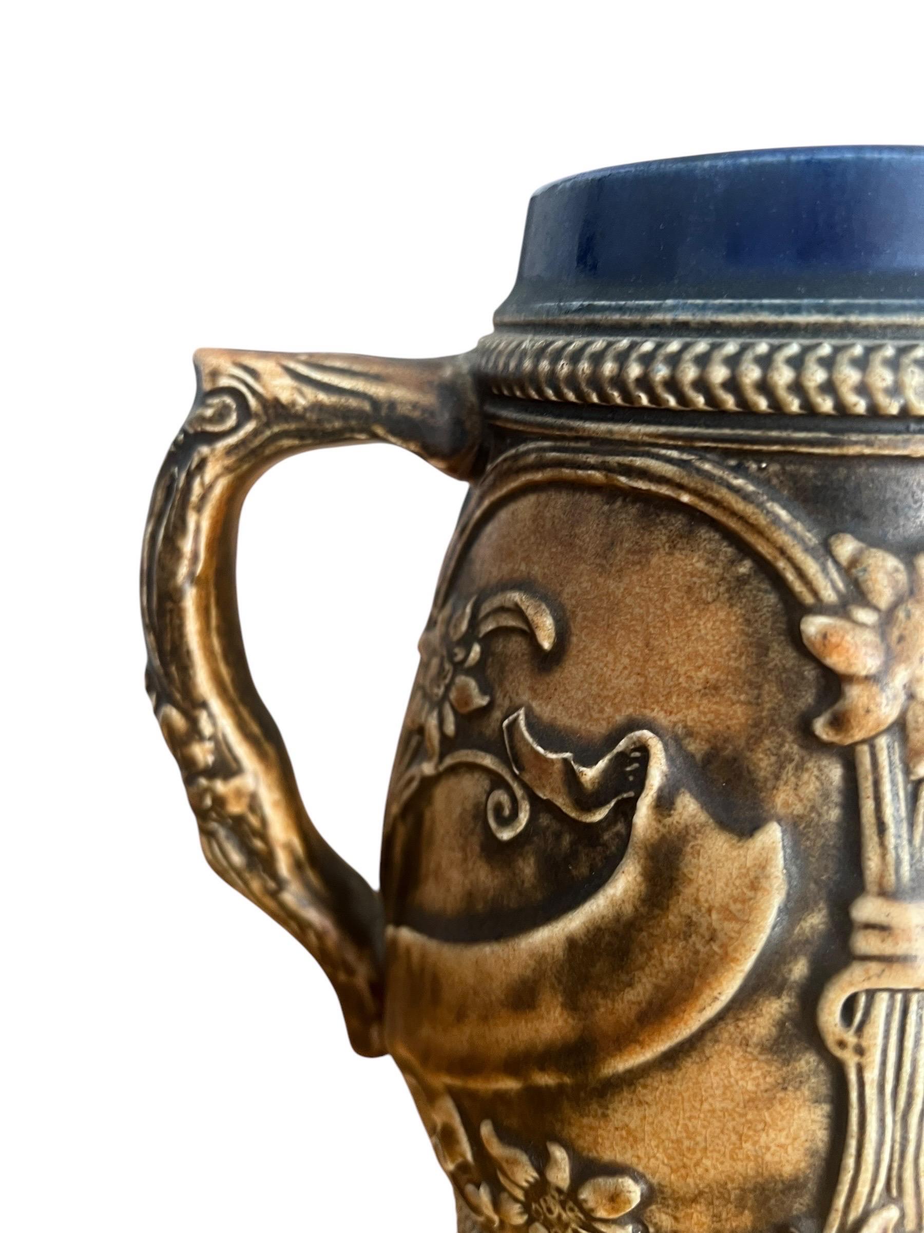 Charming German beer stein from the mid-20th century.
Ceramic stein decorated with floral designs, houses, and two German figures, a man and a woman, in the Bavarian style.
Blue and cream glazed ceramic.

A beautiful item for collectors or beer
