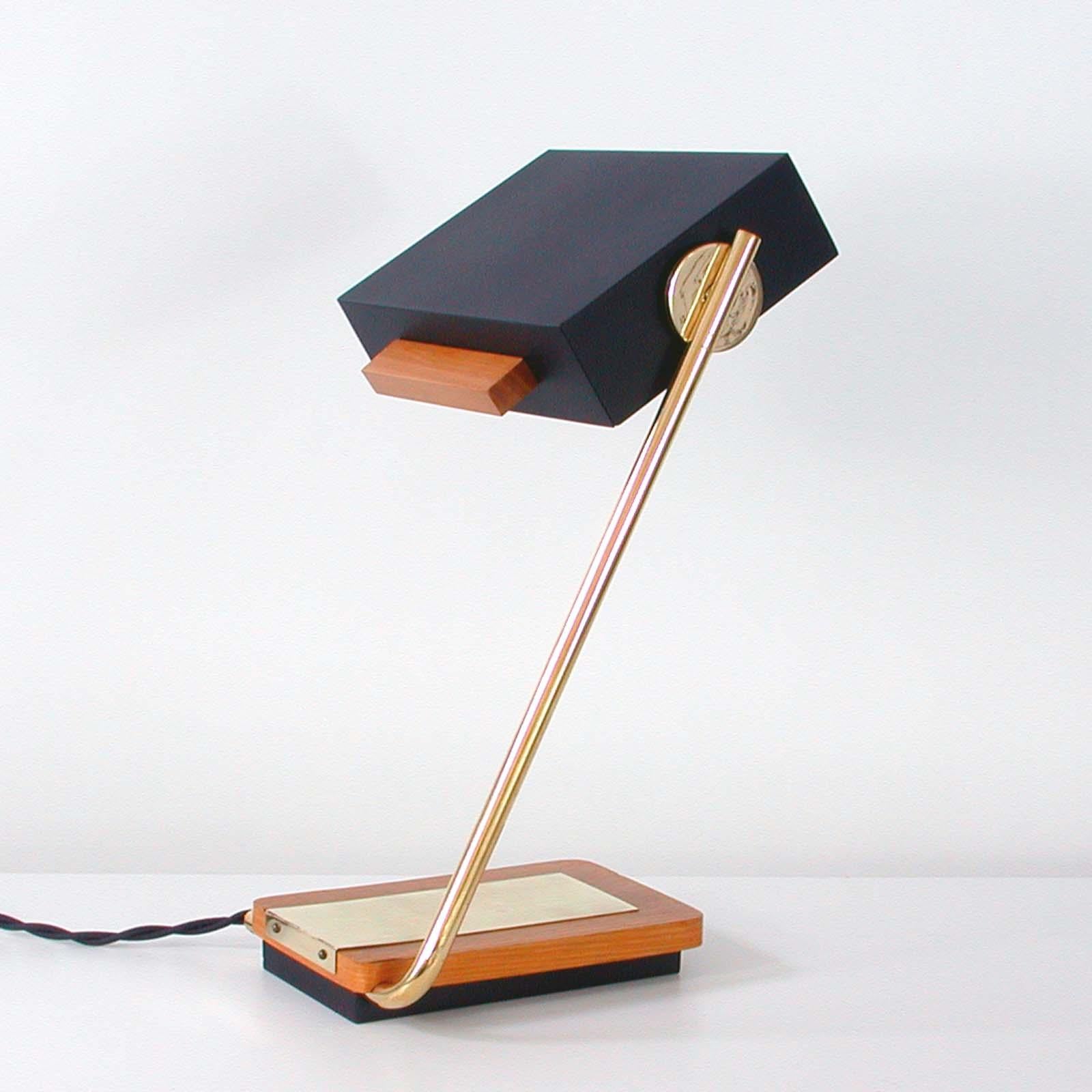 This modernist table or desk lamp was designed and manufactured in Germany in the 1960s by Kaiser Leuchten. It has got a teak base, a brass adjustable lamp arm and a black rectangular shade with an off white interior.

It requires one E14 bulb.