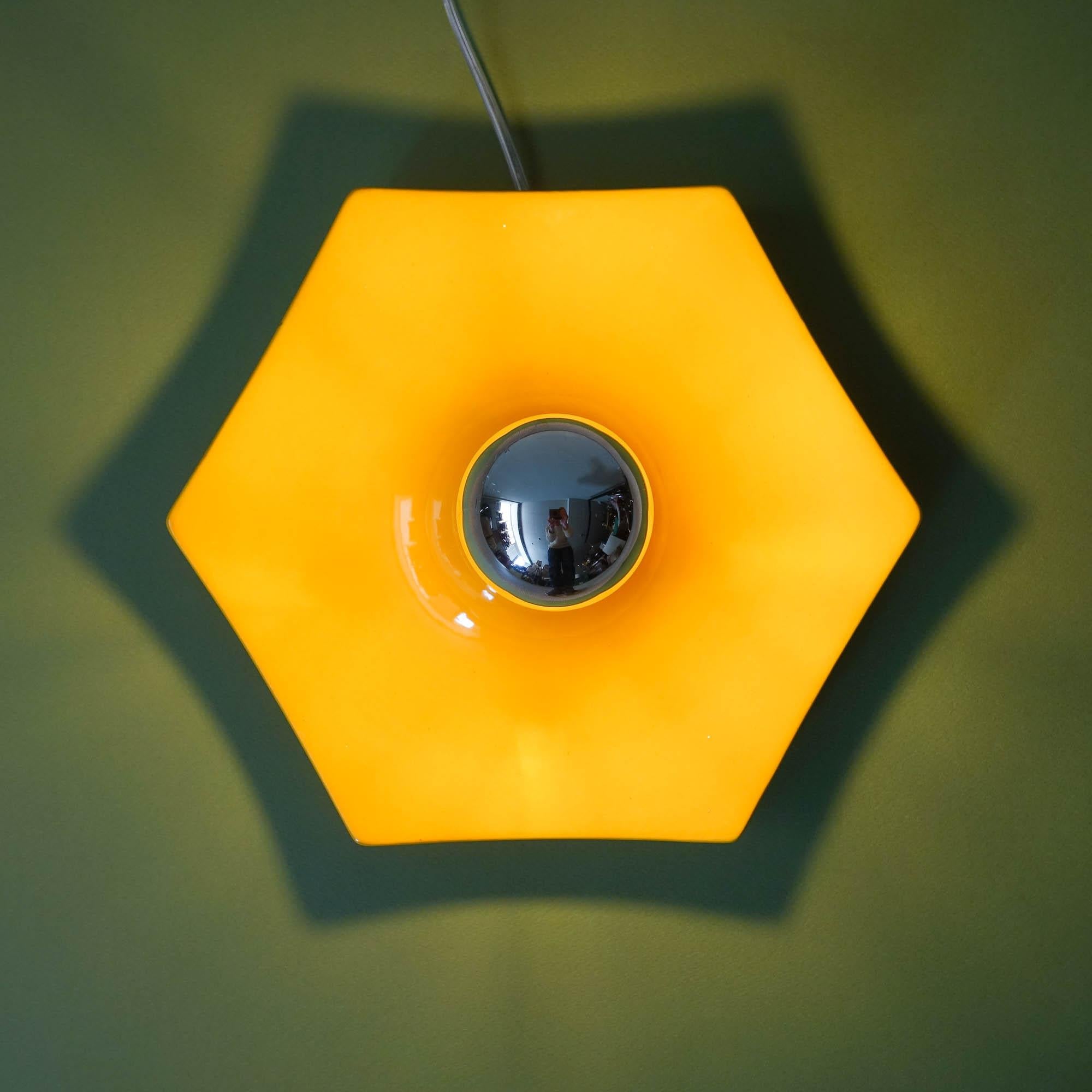 This wall lamp was designed and produced in Germany, during the 1970s. 
It is entirely formed by ceramic following a hexagonal design, with a yellow glaze. 
It takes an E27 screw mount bulb to work. Silver CAP type is preferred. 
In original and